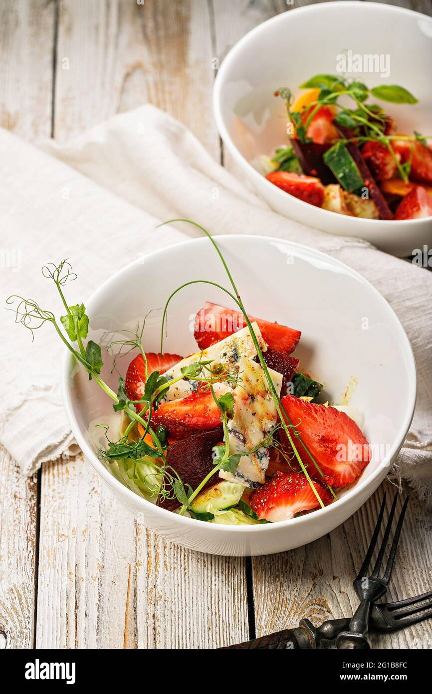 Salade d'été délicieuse prise verticale. Salade de fraises fraîches, betteraves cuites au four, tomates jaunes, fromage bleu bocal et herbes dans un bol blanc sur un bateau Banque D'Images