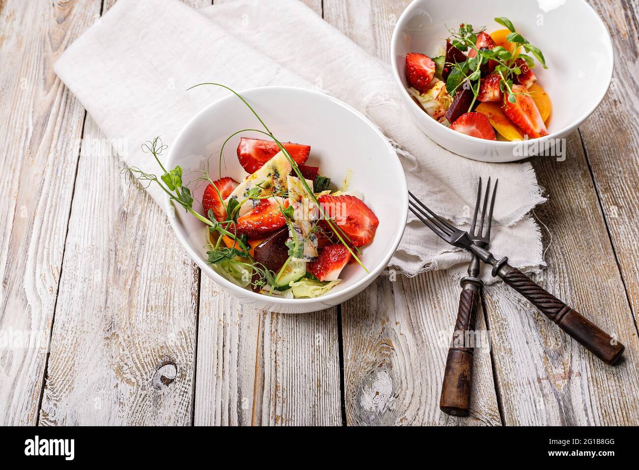 Salade d'été délicieuse. Salade de fraises fraîches, betteraves cuites au four, tomates jaunes, fromage bleu et herbes dans un bol blanc sur un filet rustique léger Banque D'Images