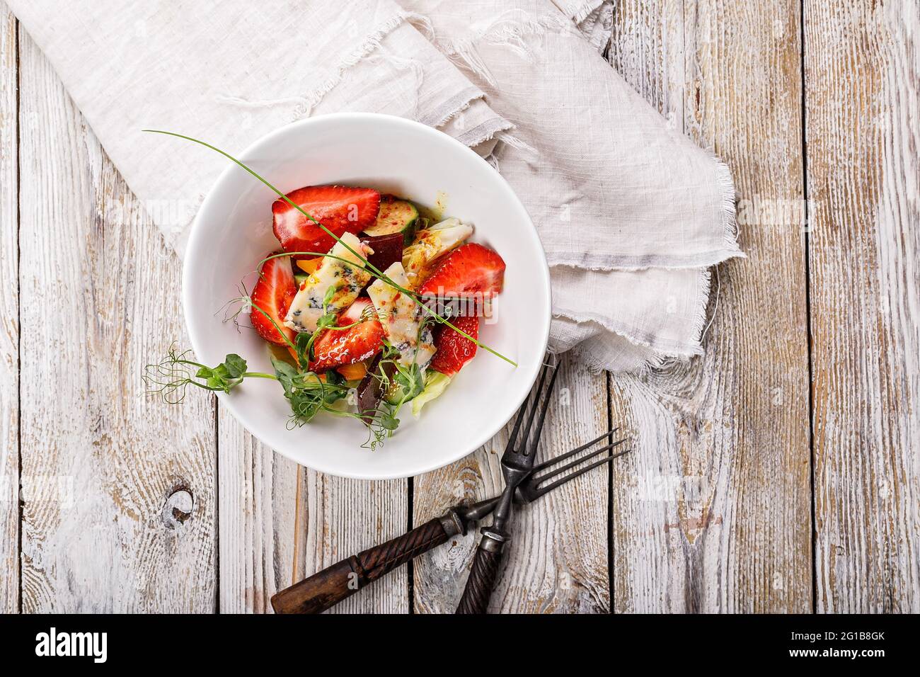 Salade d'été délicieuse. Salade de fraises fraîches, betteraves cuites au four, tomates jaunes, fromage bleu et herbes dans un bol blanc sur un filet rustique léger Banque D'Images