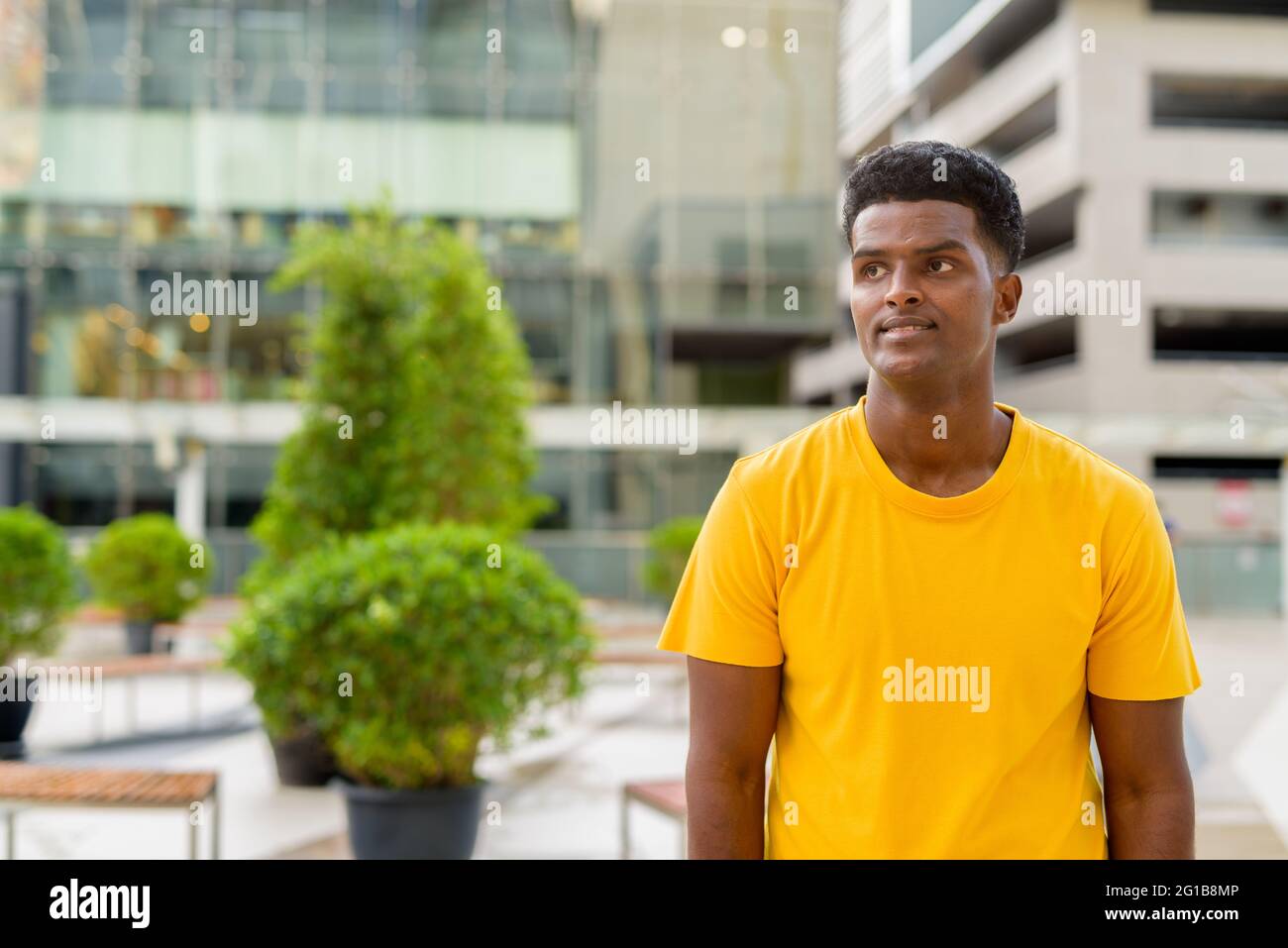 Portrait d'un beau homme africain noir portant un t-shirt jaune à l'extérieur de la ville pendant l'été tout en pensant Banque D'Images