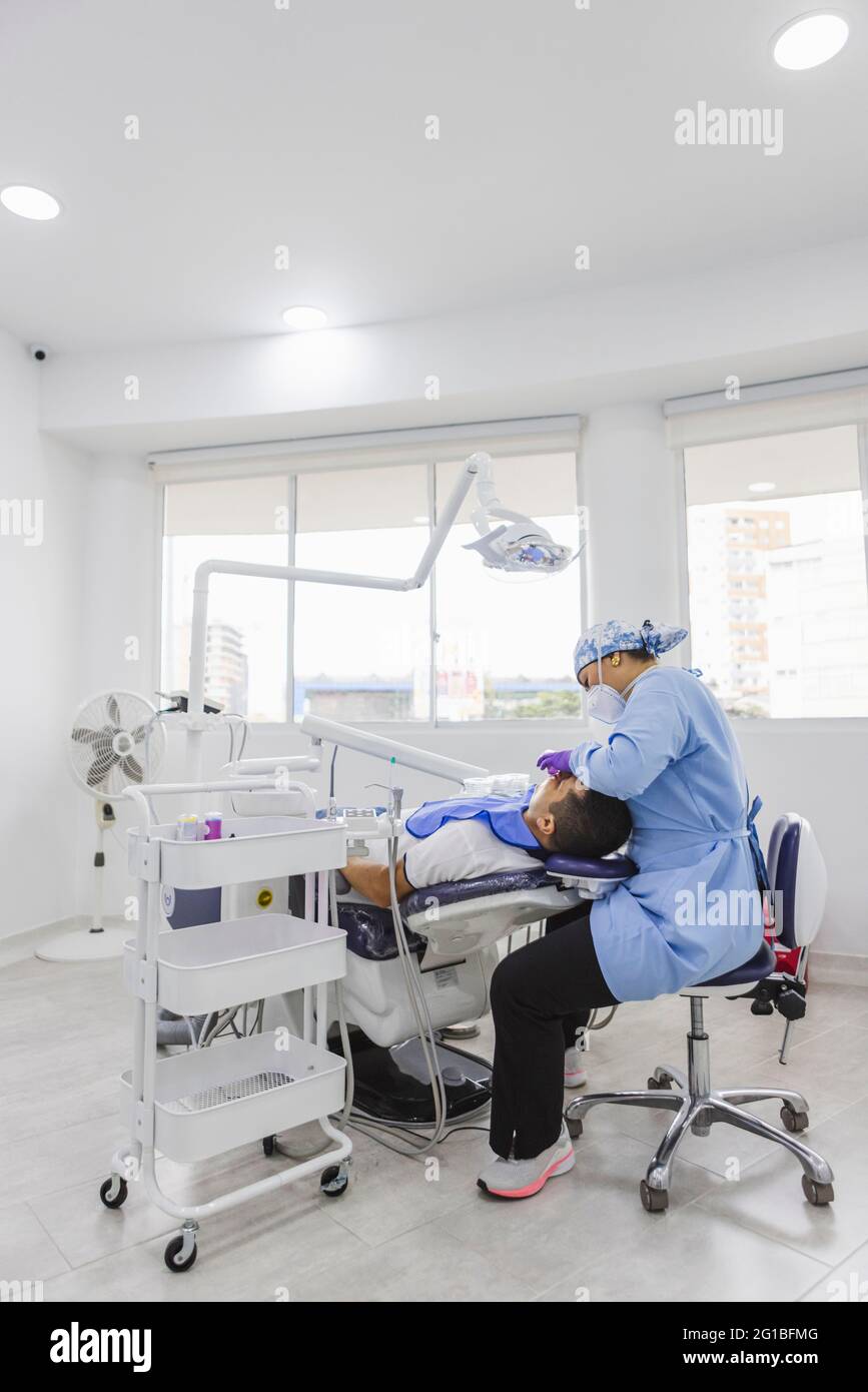 Vue latérale d'une femme médecin dans les dents de nettoyage uniformes d'un patient de sexe masculin avec enrouleur dentaire à l'hôpital Banque D'Images Vue latérale d'une femme médecin dans les dents de nettoyage uniformes d'un patient de sexe masculin avec enrouleur dentaire à l'hôpital Banque D'Images