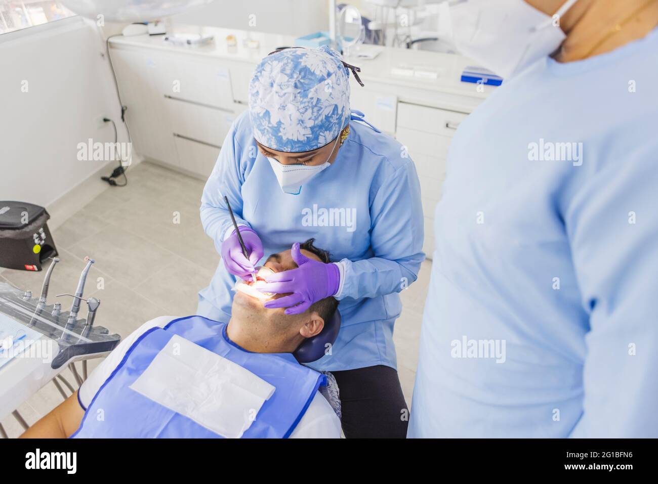 Par dessus le médecin anonyme de sexe féminin dans les dents de nettoyage uniforme de la patiente masculine avec enrouleur dentaire à l'hôpital Banque D'Images Par dessus le médecin anonyme de sexe féminin dans les dents de nettoyage uniforme de la patiente masculine avec enrouleur dentaire à l'hôpital Banque D'Images