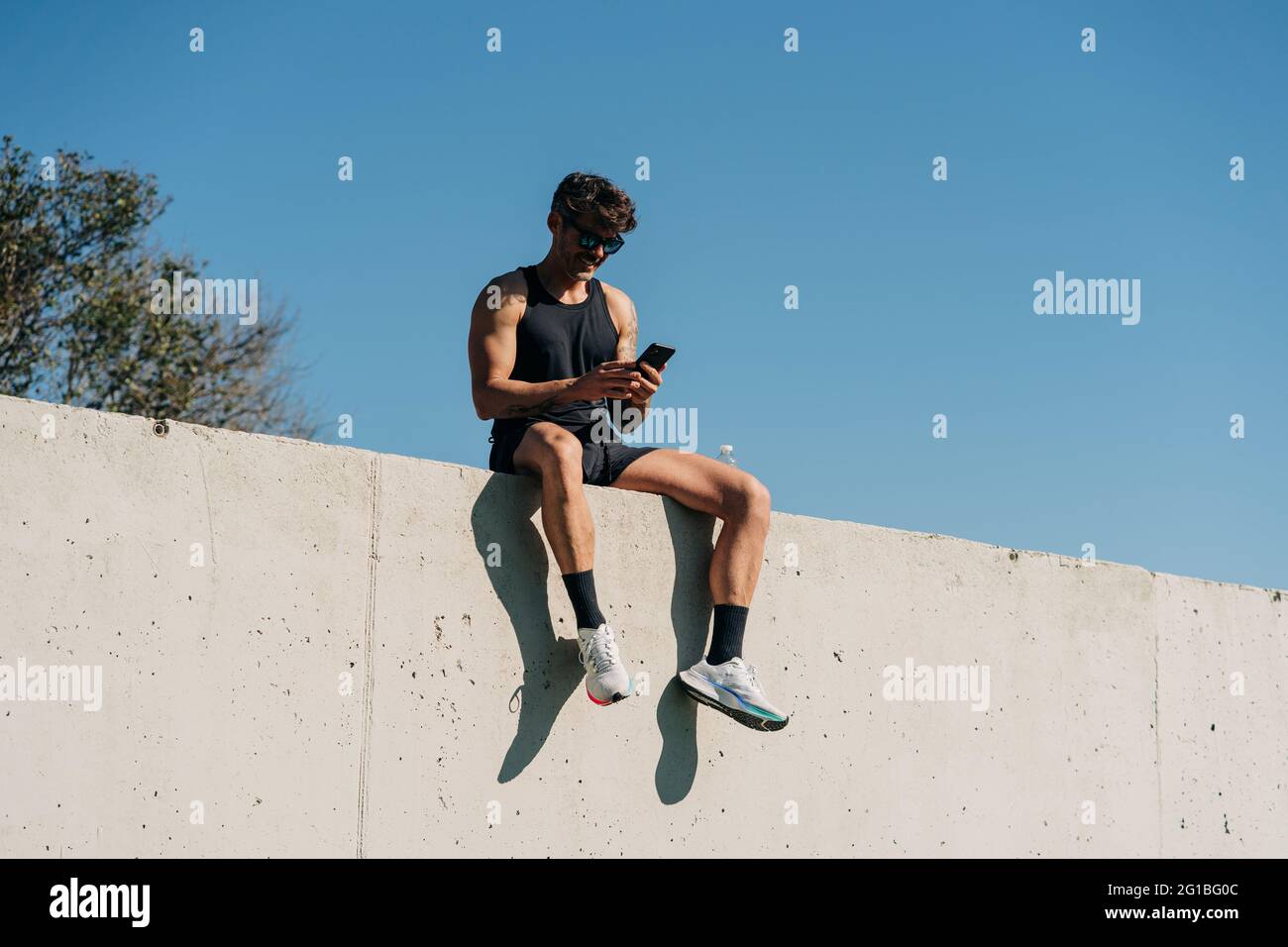 Posez l'athlète masculin dans les vêtements de sport en parcourant le téléphone portable tout en vous reposant sur la clôture après l'entraînement Banque D'Images