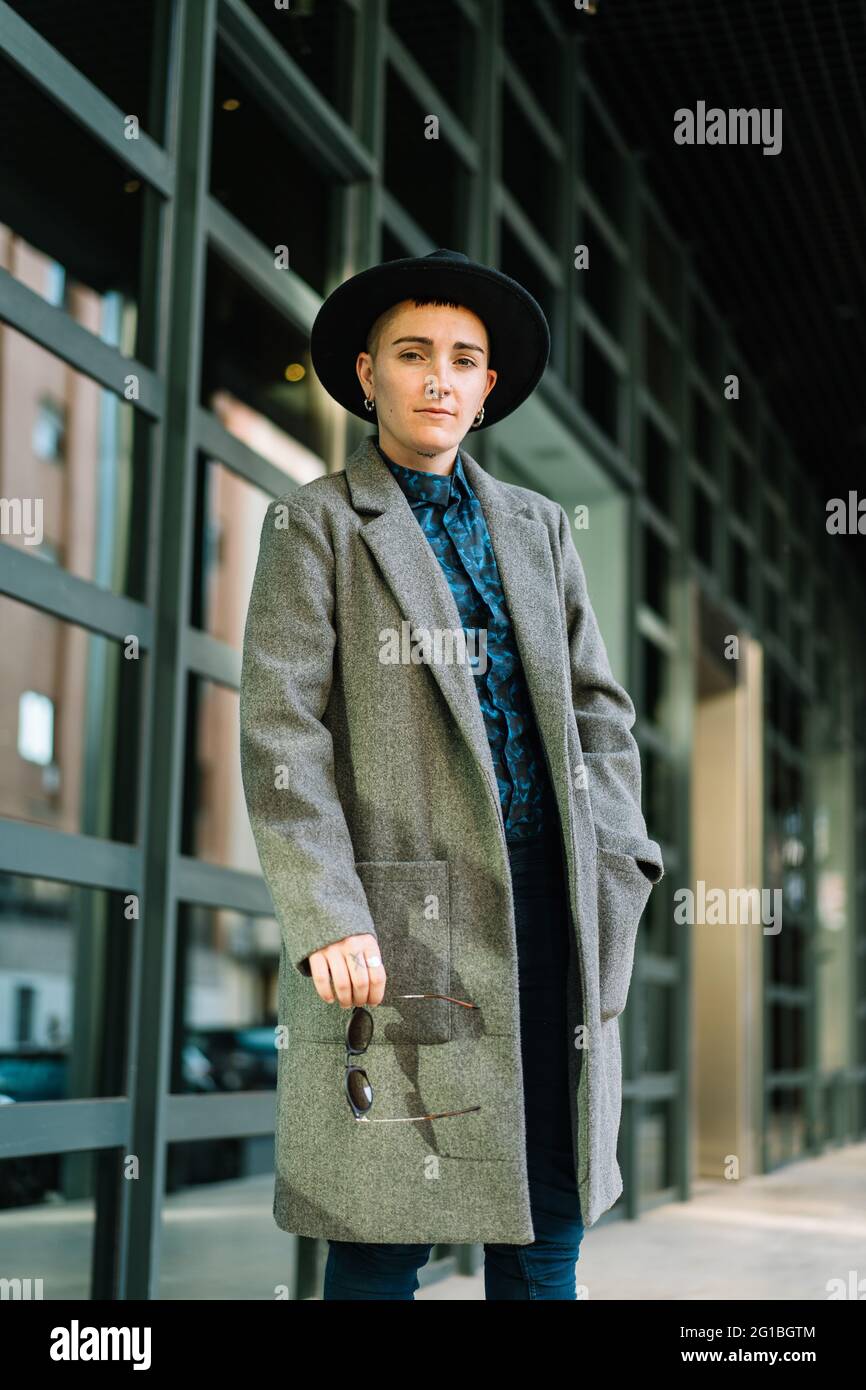 Jeune homme transgenre en manteau classe et chapeau regardant la caméra à  la lumière du jour Photo Stock - Alamy