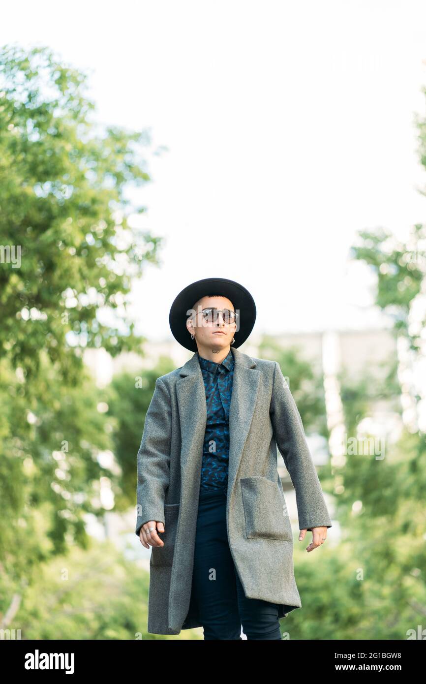 Jeune homme transgenre en manteau classe et chapeau regardant loin dans la  lumière du jour Photo Stock - Alamy