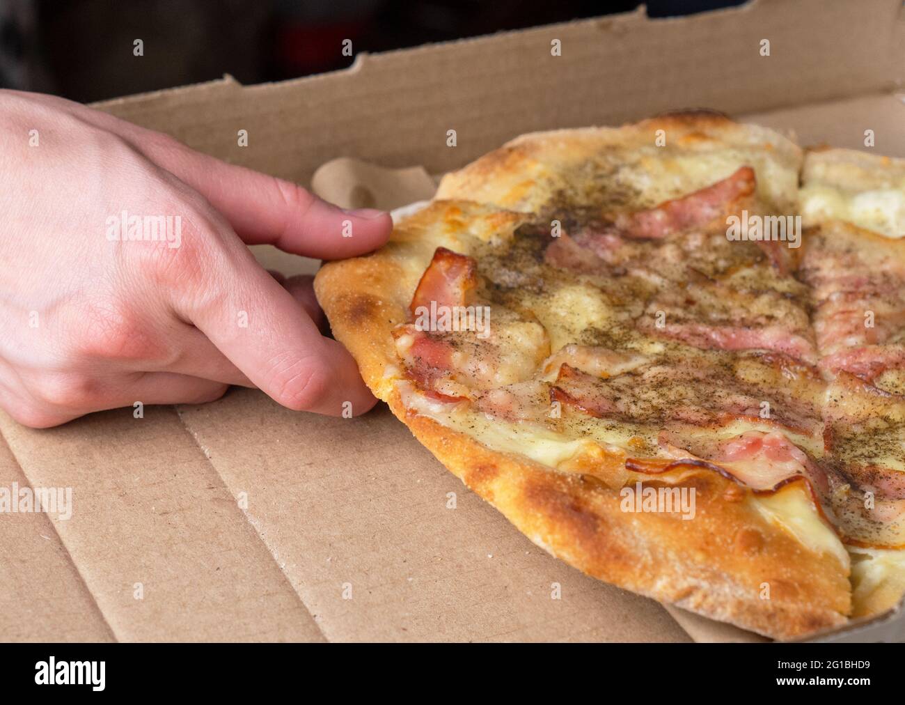La main d'une femme prend une tranche de pizza avec du bacon. Gros plan. Banque D'Images