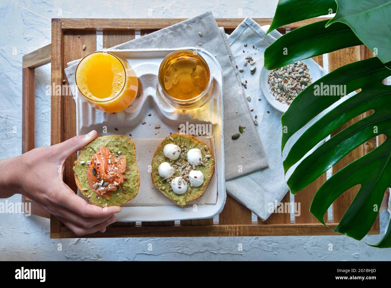 Vue de dessus de la récolte personne méconnaissable mangeant appétissant des toasts d'avocat sains avec du saumon et du fromage burrata servis sur le plateau avec des verres de ju frais Banque D'Images