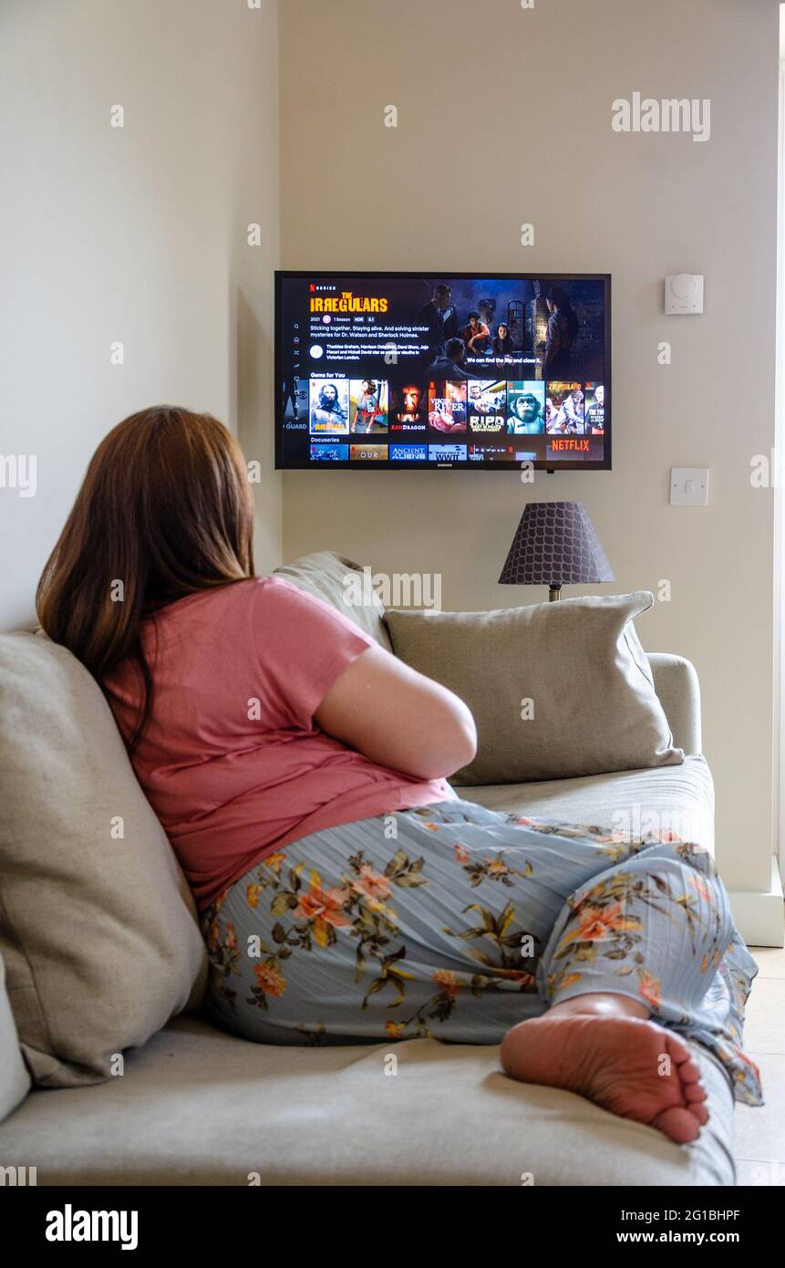 Une dame se détend sur un canapé et sélectionne un film à regarder sur Netflix. Diffusé à la télévision sur Internet. Banque D'Images