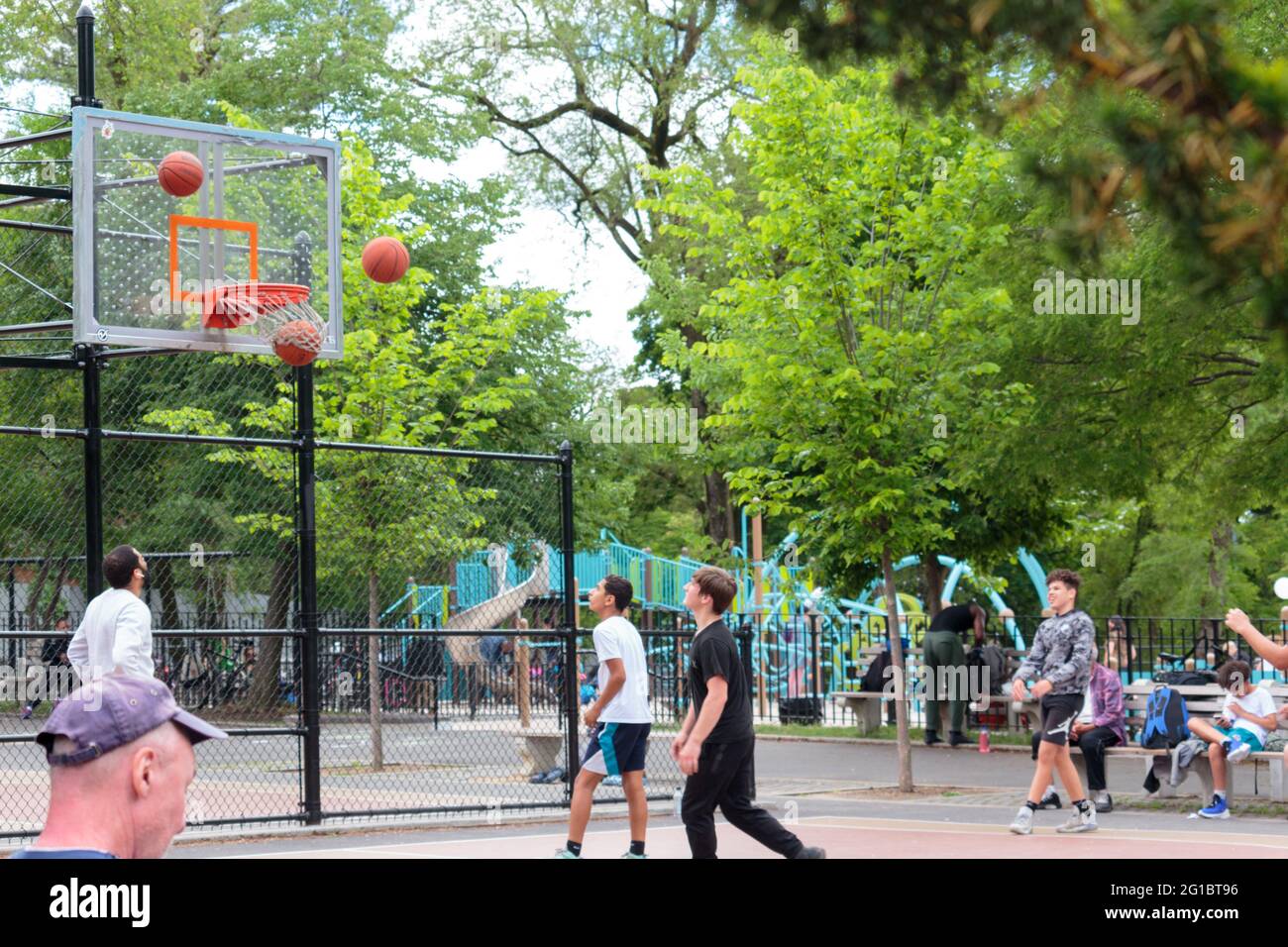 plusieurs ballons de basket-ball volent dans les airs vers le panier pendant que l'on entre pour marquer sur un terrain de basket-ball de la ville de new york, en tant que jeunes joueurs l Banque D'Images