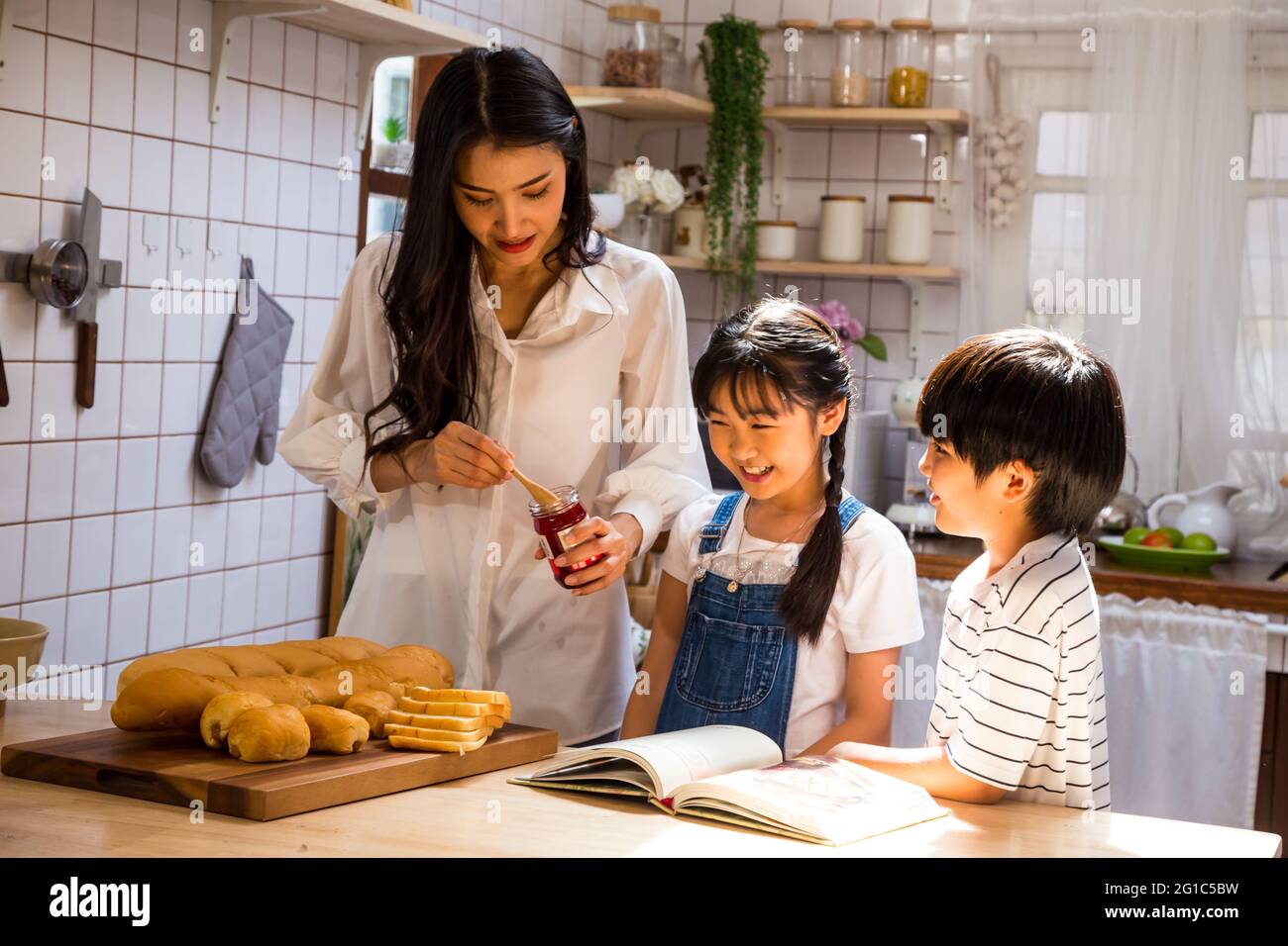 Famille asiatique faisant la nourriture de petit déjeuner avec du pain dans la cuisine à la maison en vacances. Mère et fils souriants et fille cuisinant ensemble et heureux activi Banque D'Images