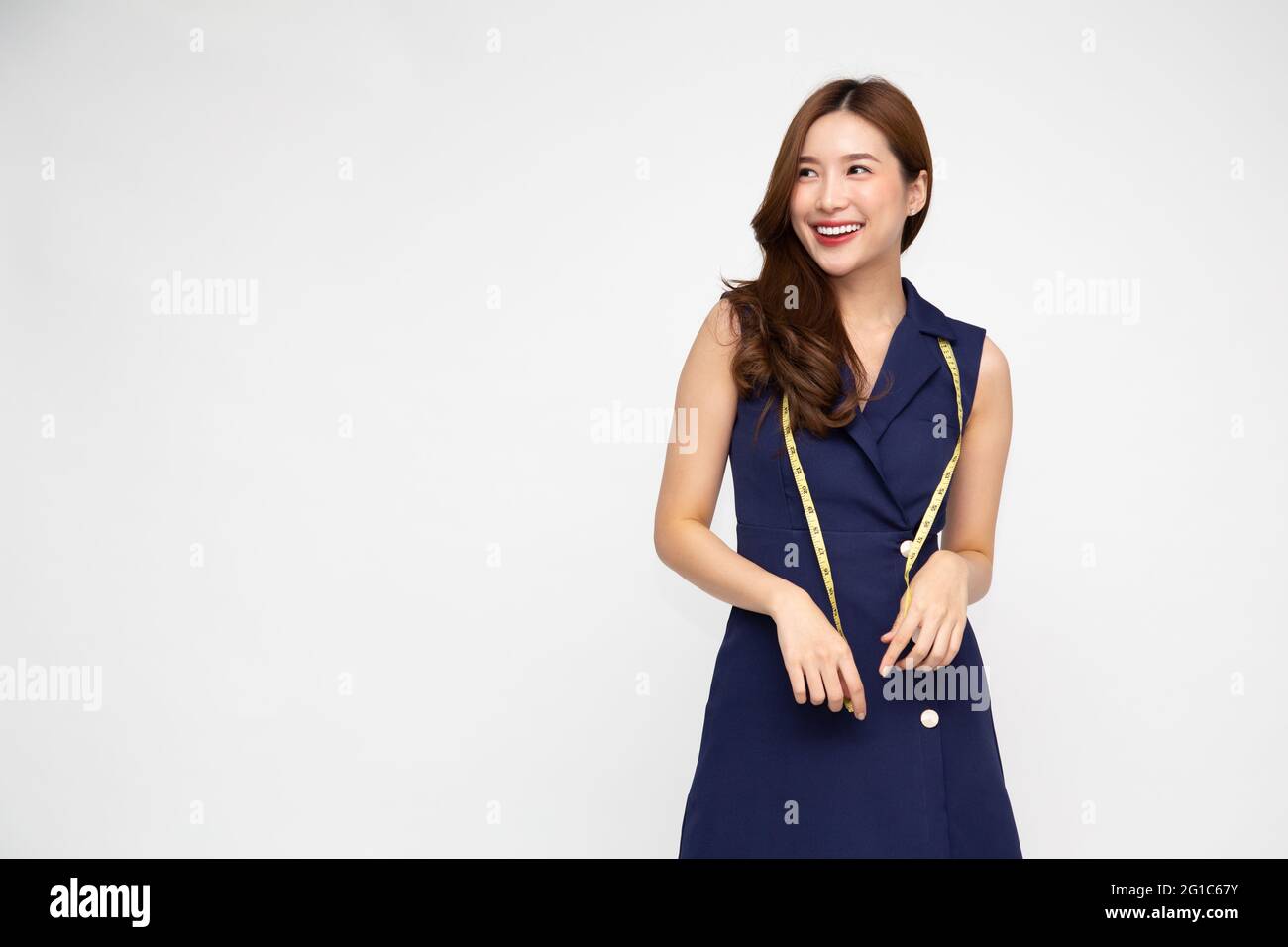 Portrait d'une femme vêtements de designer de mode dans une robe bleu profond avec ruban de mesure isolé sur fond blanc, modèle asiatique élégant féminin Banque D'Images