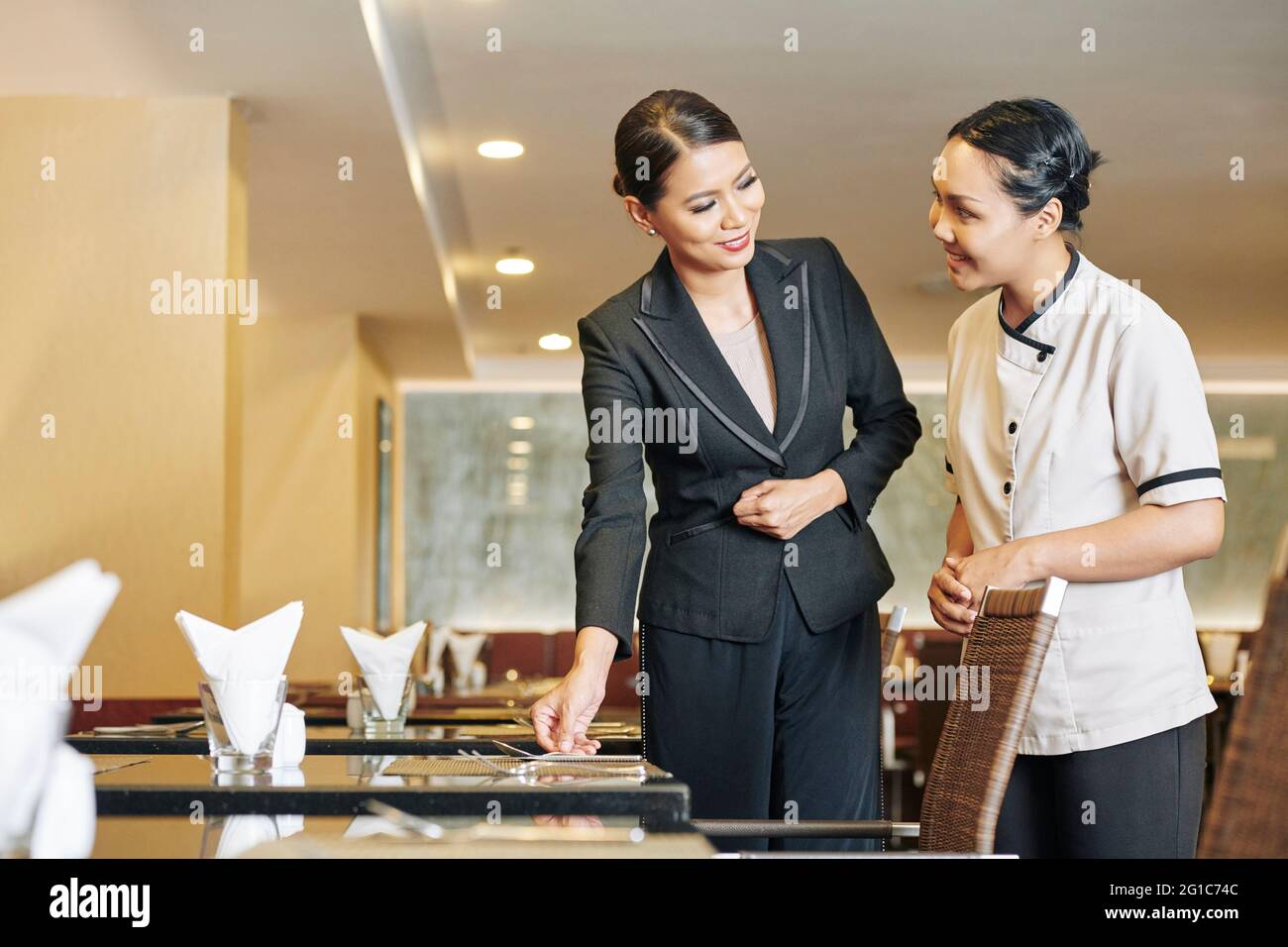 Un gérant souriant explique à la serveuse comment placer les couverts et les plats raffinés sur les tables Banque D'Images