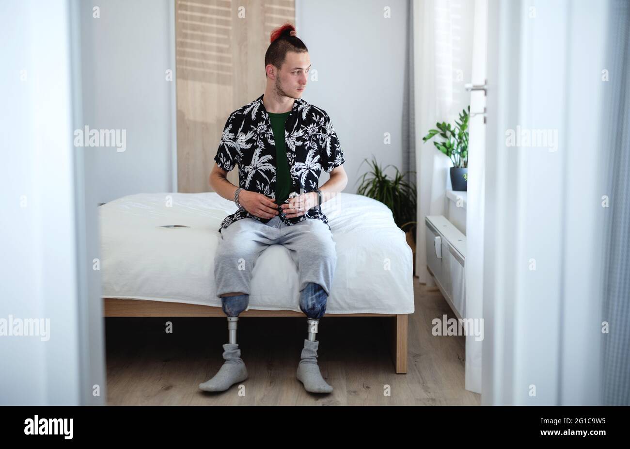 Portrait d'un jeune homme handicapé assis au lit à l'intérieur à la maison, concept prothétique de jambe. Banque D'Images