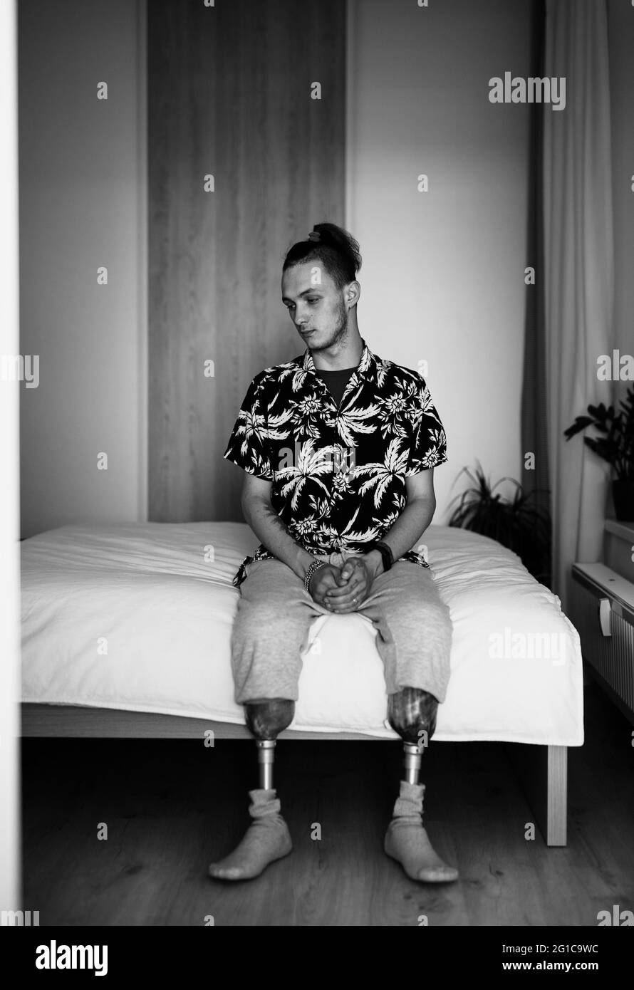 Portrait noir et blanc du jeune homme handicapé assis au lit à l'intérieur à la maison, concept prothétique de jambe. Banque D'Images