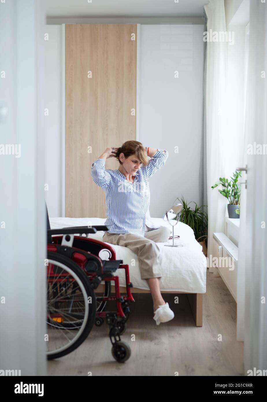 Femme adulte handicapée assise sur le lit à l'intérieur à la maison, routine du matin avec le concept de jambe amputée. Banque D'Images