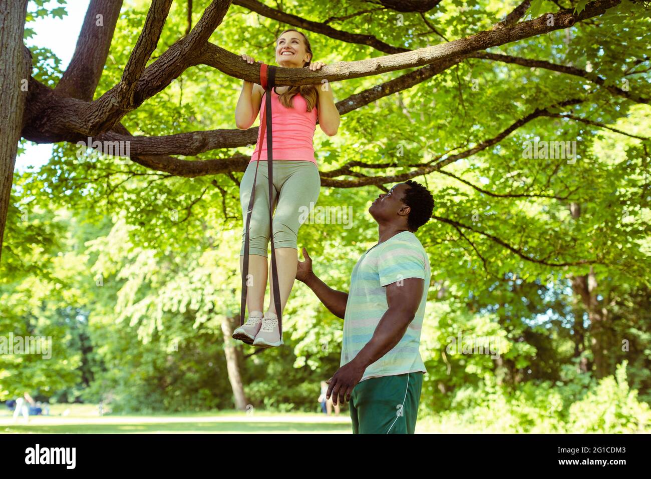 Femme faisant le pull-up assistée par son entraîneur de fitness sur l'arbre Banque D'Images
