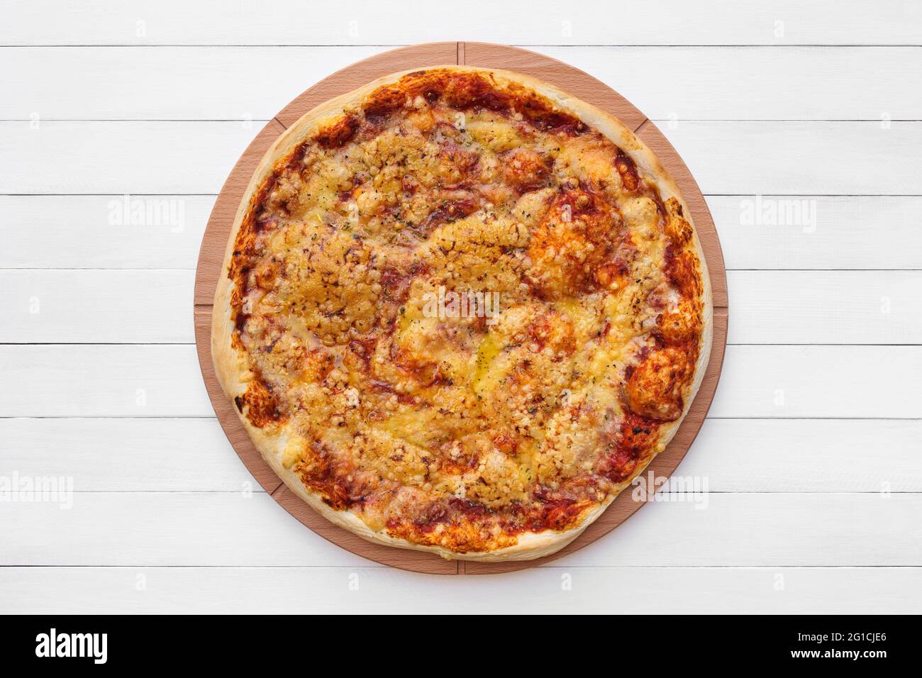 Pizza ronde complète recouverte de fromage et d'origan sur une assiette en bois. Vue de dessus sur fond de tableau blanc Banque D'Images