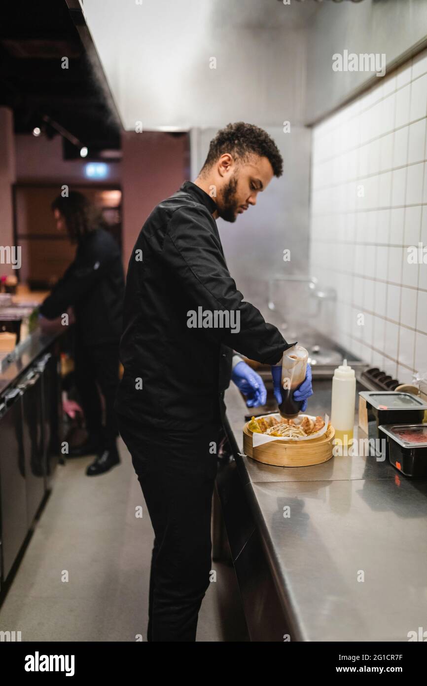 Un jeune serveur de sexe masculin prépare la nourriture au restaurant Banque D'Images