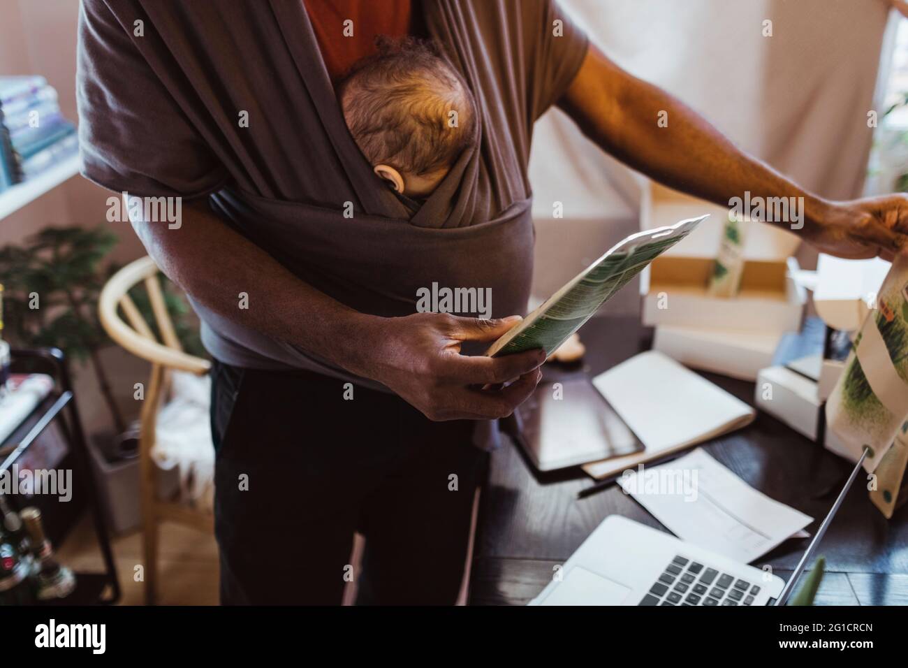 Section médiane de l'ensemble de maintien professionnel masculin avec fils dans un porte-bébé au bureau à domicile Banque D'Images