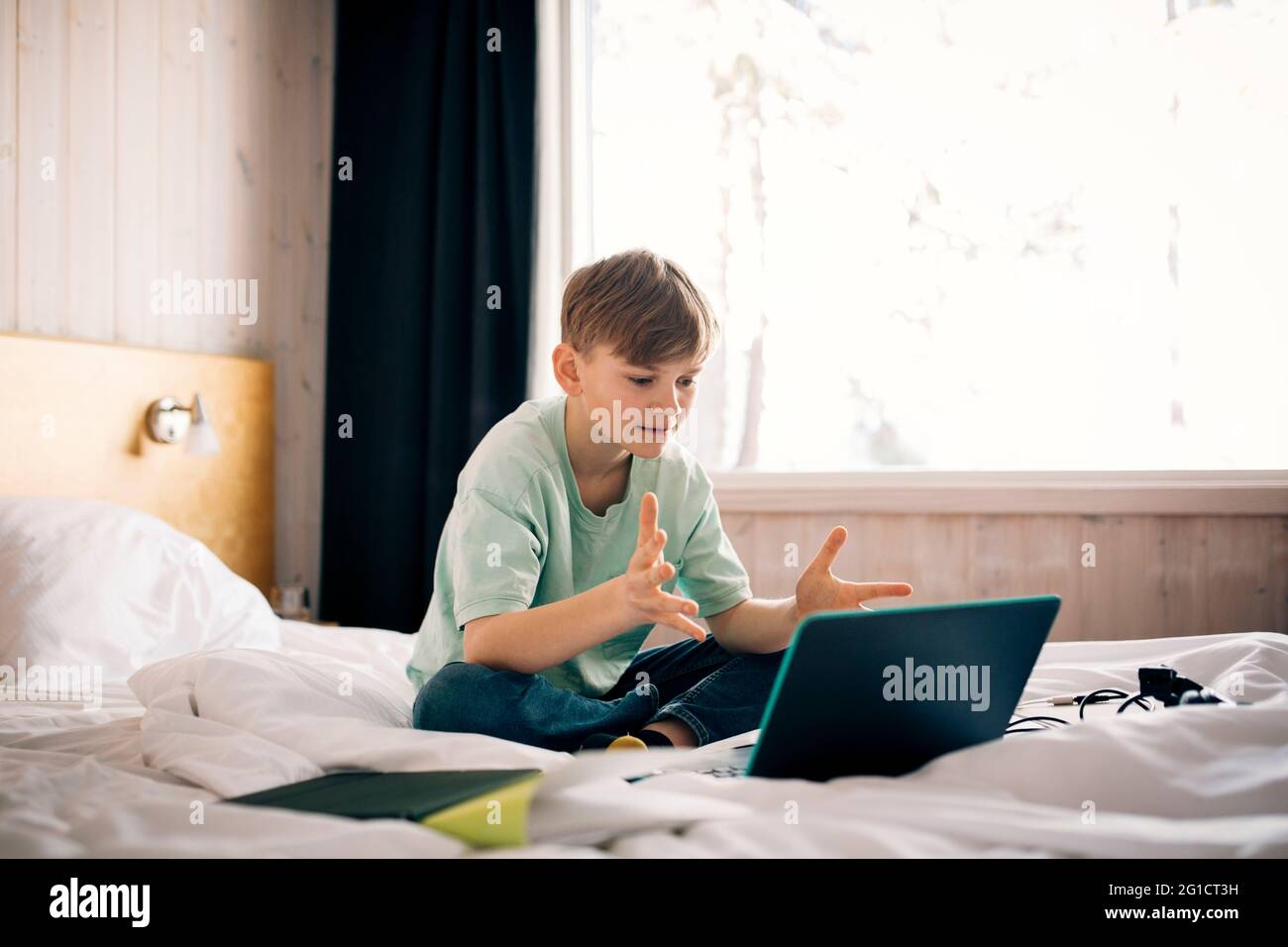 Garçon assistant à un appel vidéo tout en faisant des gestes pendant la maison dans la chambre à coucher Banque D'Images