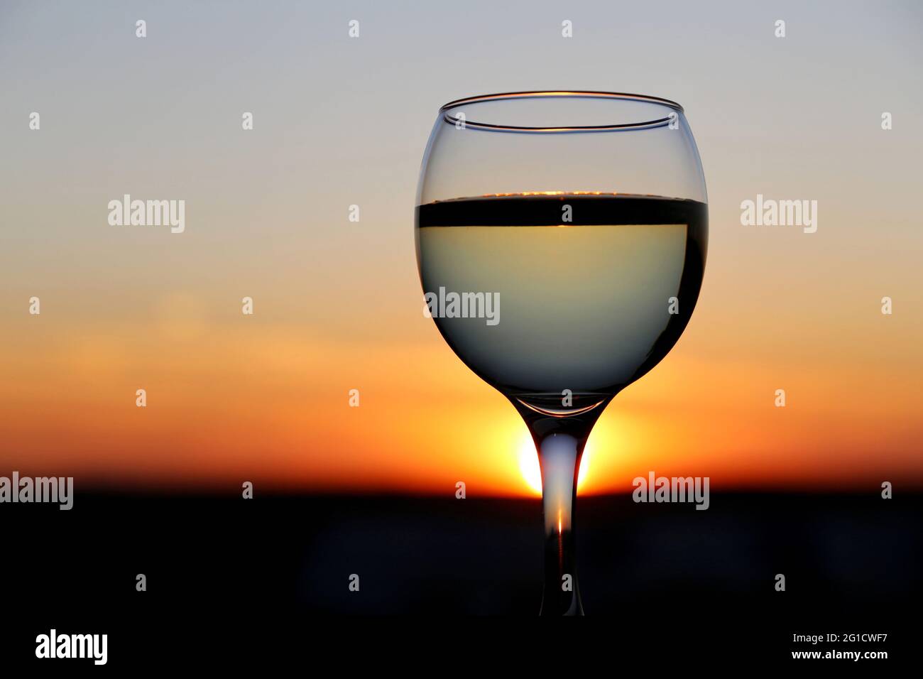 Verre à vin blanc sur fond coucher de soleil magnifique, et le ciel se reflètent dans l'alcool boire. Concept de soirée de célébration, de resort Banque D'Images