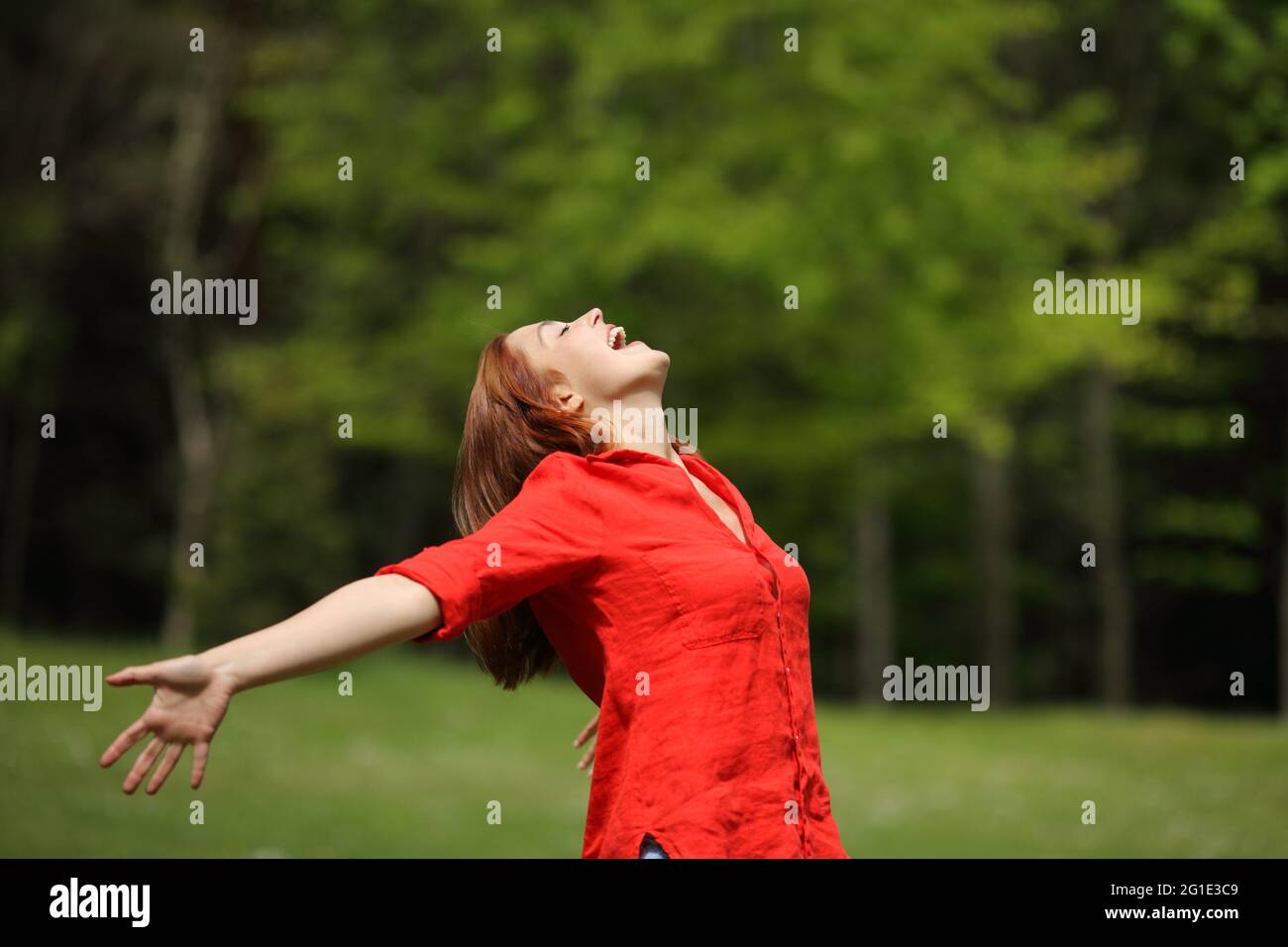 Femme excitée en rouge criant à l'air étirant les bras dans une forêt Banque D'Images