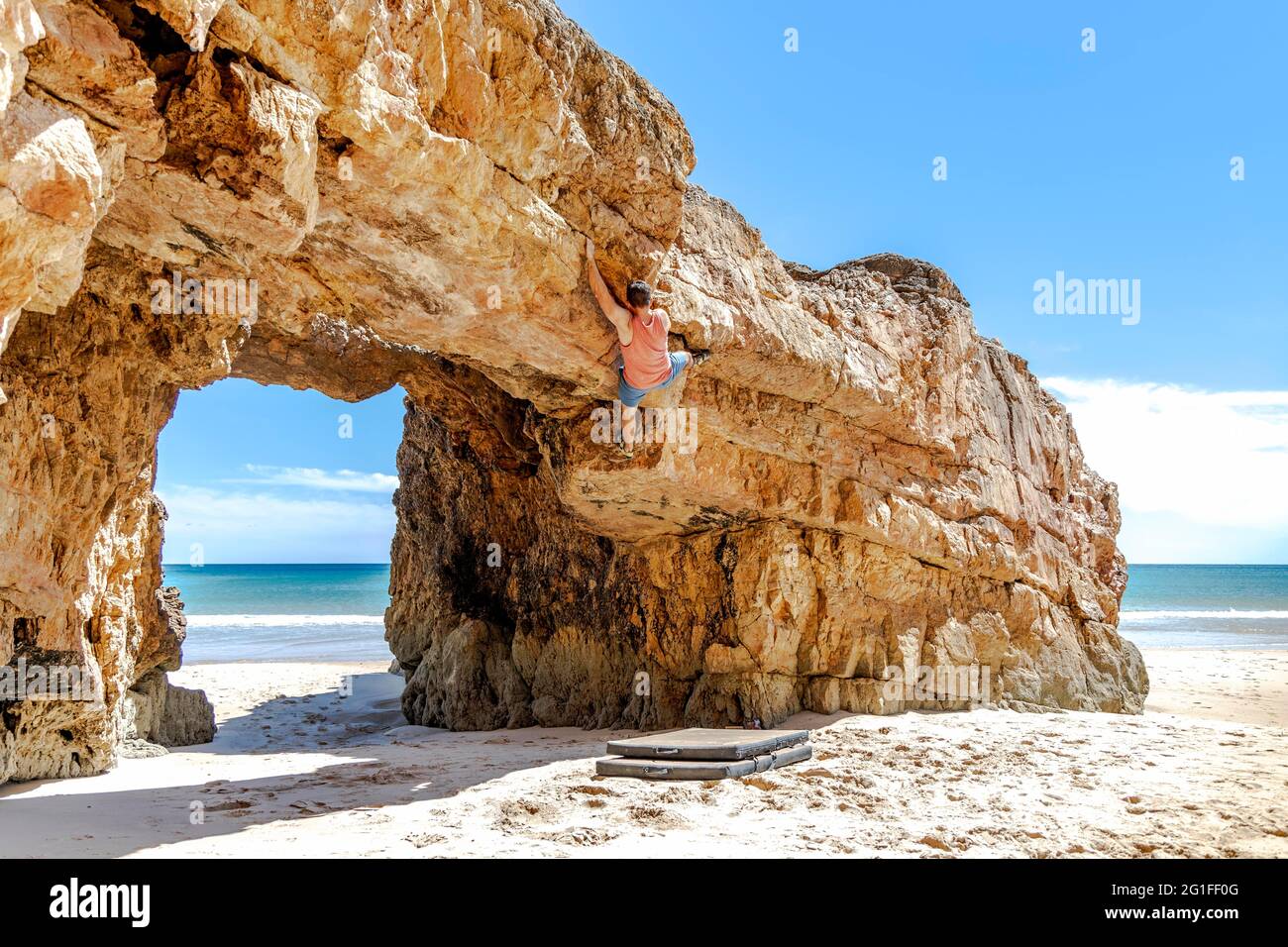 Un jeune grimpeur en toute sécurité escalade une falaise jaune en Algarve, au Portugal Banque D'Images