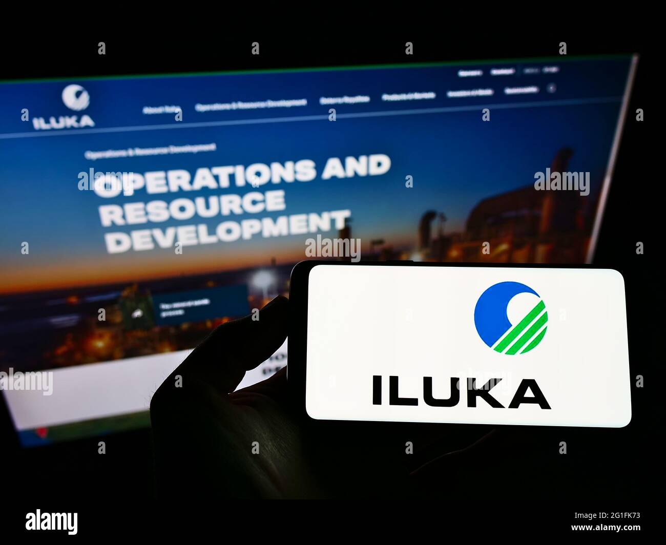 Personne tenant un téléphone portable avec le logo de la société minière australienne Iluka Resources Limited à l'écran en face de la page Web. Mise au point sur l'affichage du téléphone. Banque D'Images