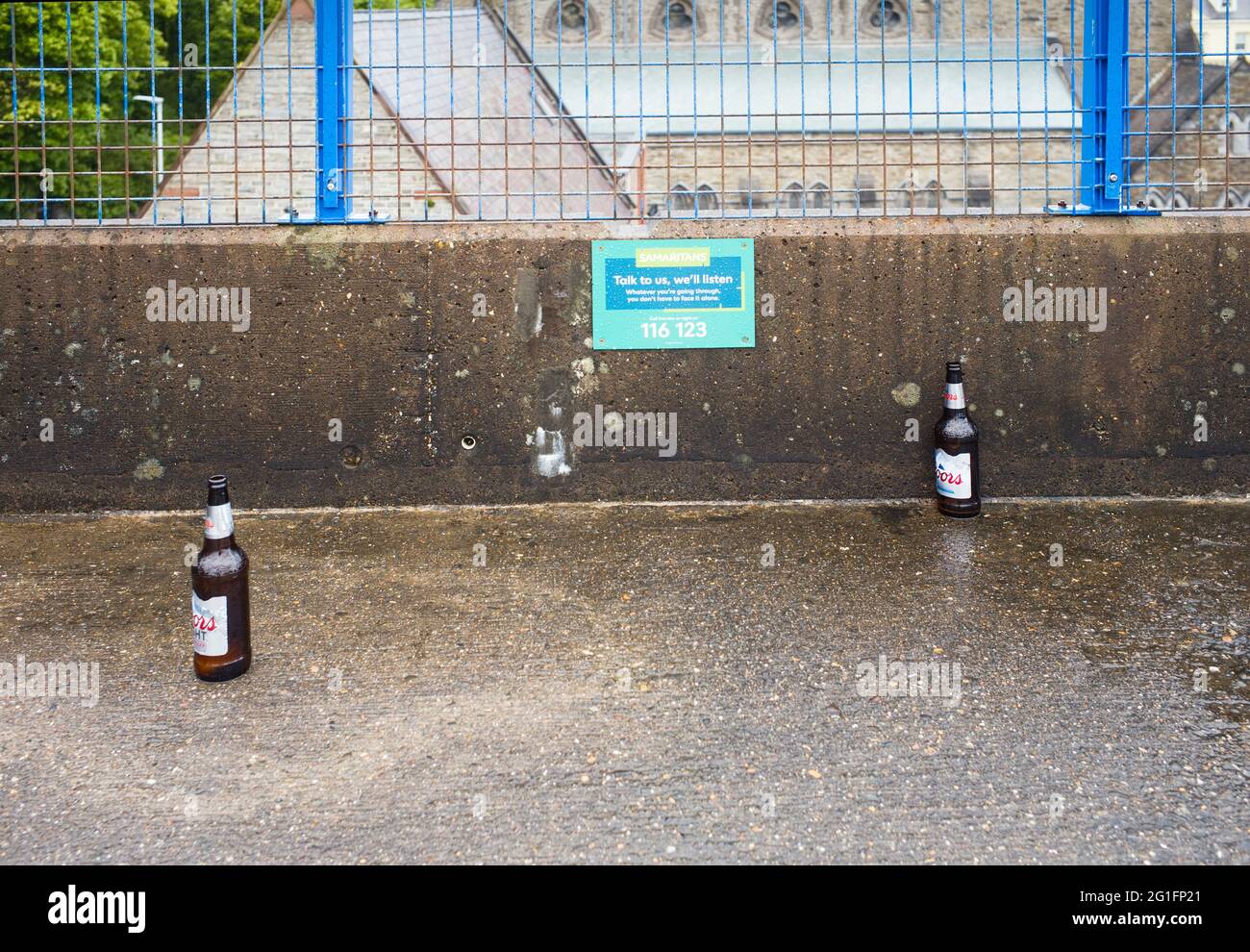 Deux bouteilles de bière vides dans un parking à côté d'un panneau Samaritans Banque D'Images