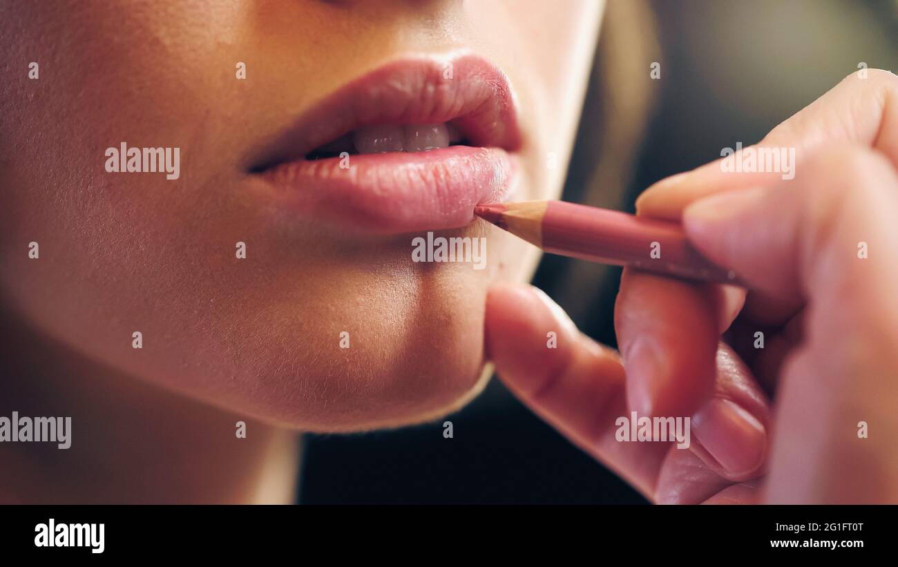 vue rognée d'un maquilleur appliquant un crayon à lèvres sur les lèvres d'une jeune femme Banque D'Images