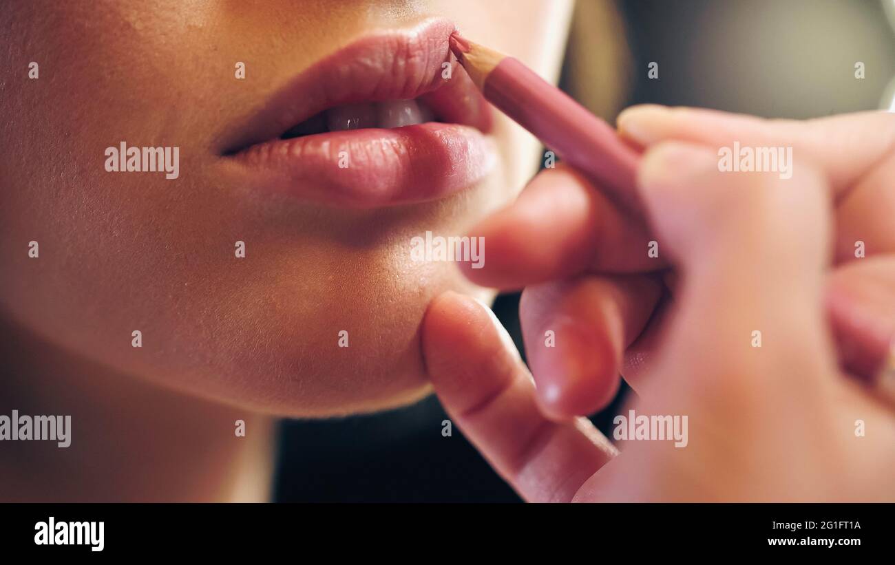 vue partielle d'un maquilleur appliquant un crayon à lèvres sur les lèvres du modèle Banque D'Images