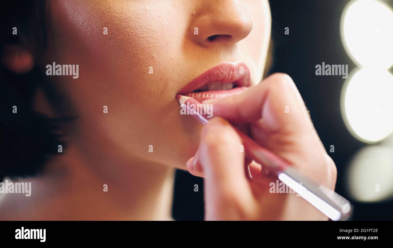 vue rognée d'un maquilleur flou artiste appliquant un crayon à lèvres sur les lèvres de la femme Banque D'Images