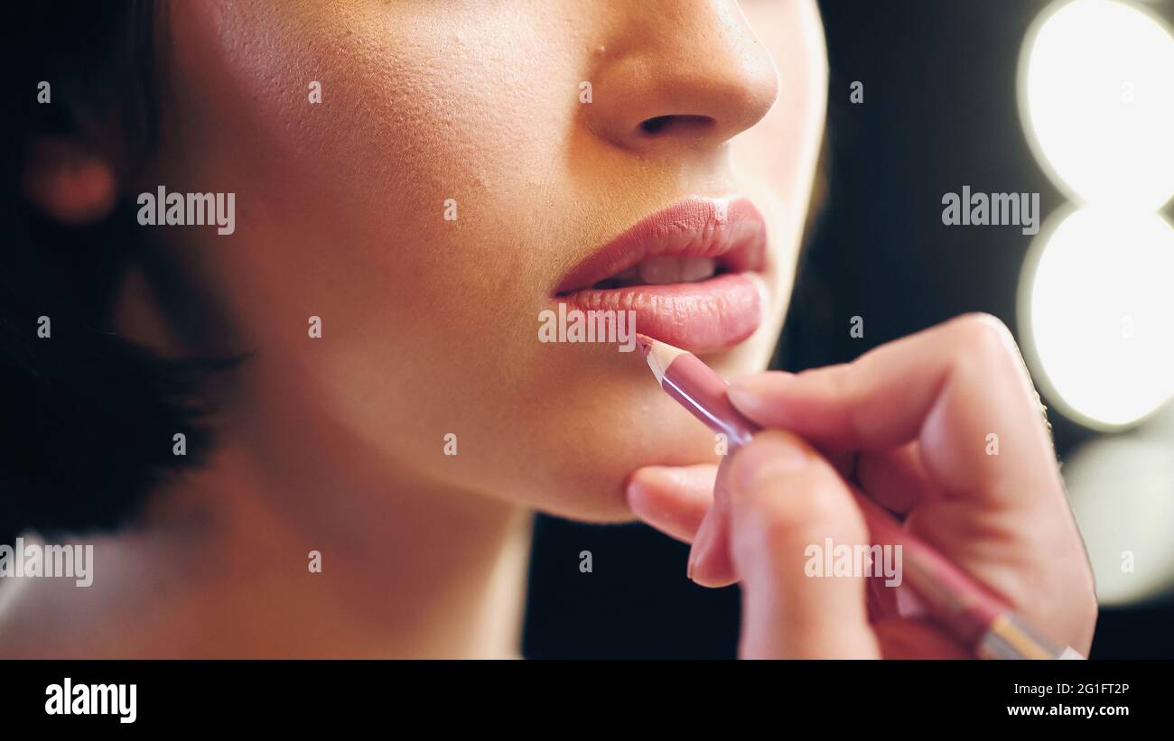 vue rognée d'un maquilleur appliquant un crayon à lèvres sur les lèvres d'une jeune femme Banque D'Images