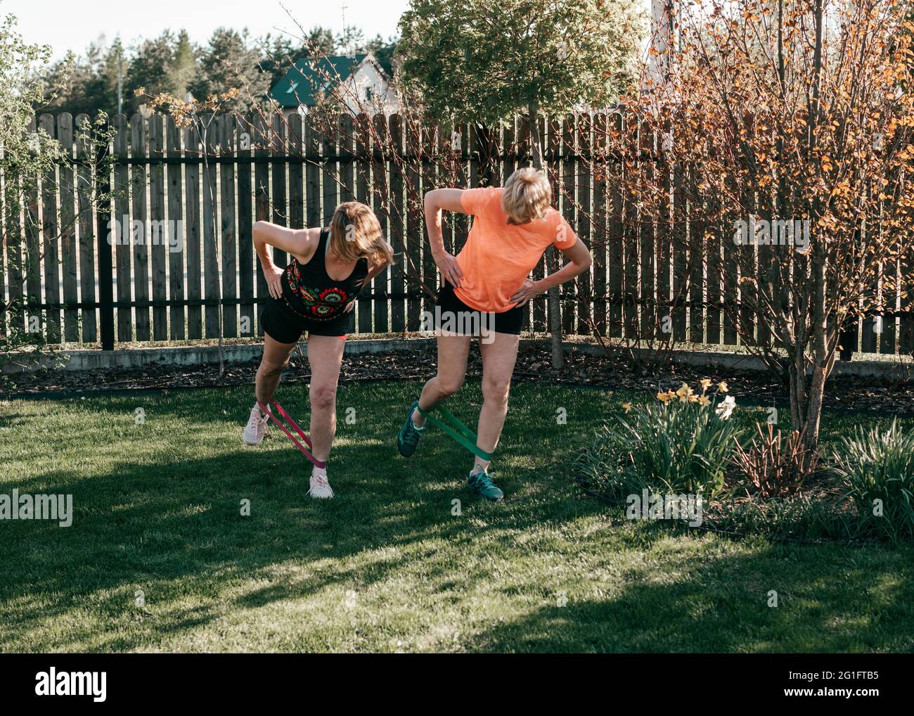 Les femmes âgées actives de 55-59 ans effectuent des exercices sur les jambes avec des élastiques de sport à l'extérieur Banque D'Images