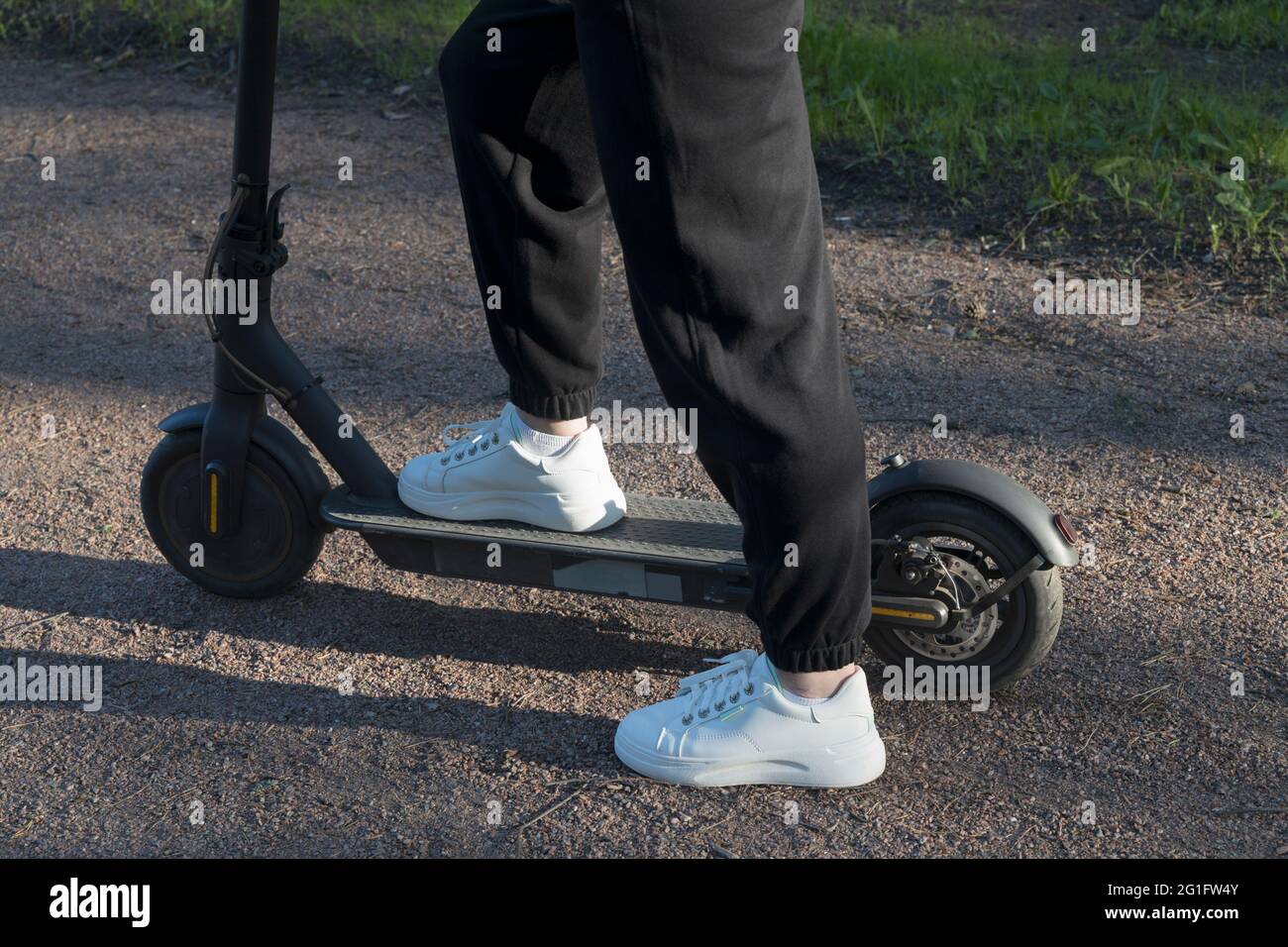 Une jeune femme se tient sur un kick scooter avec des baskets blanches et des pantalons noirs dans le profil Banque D'Images