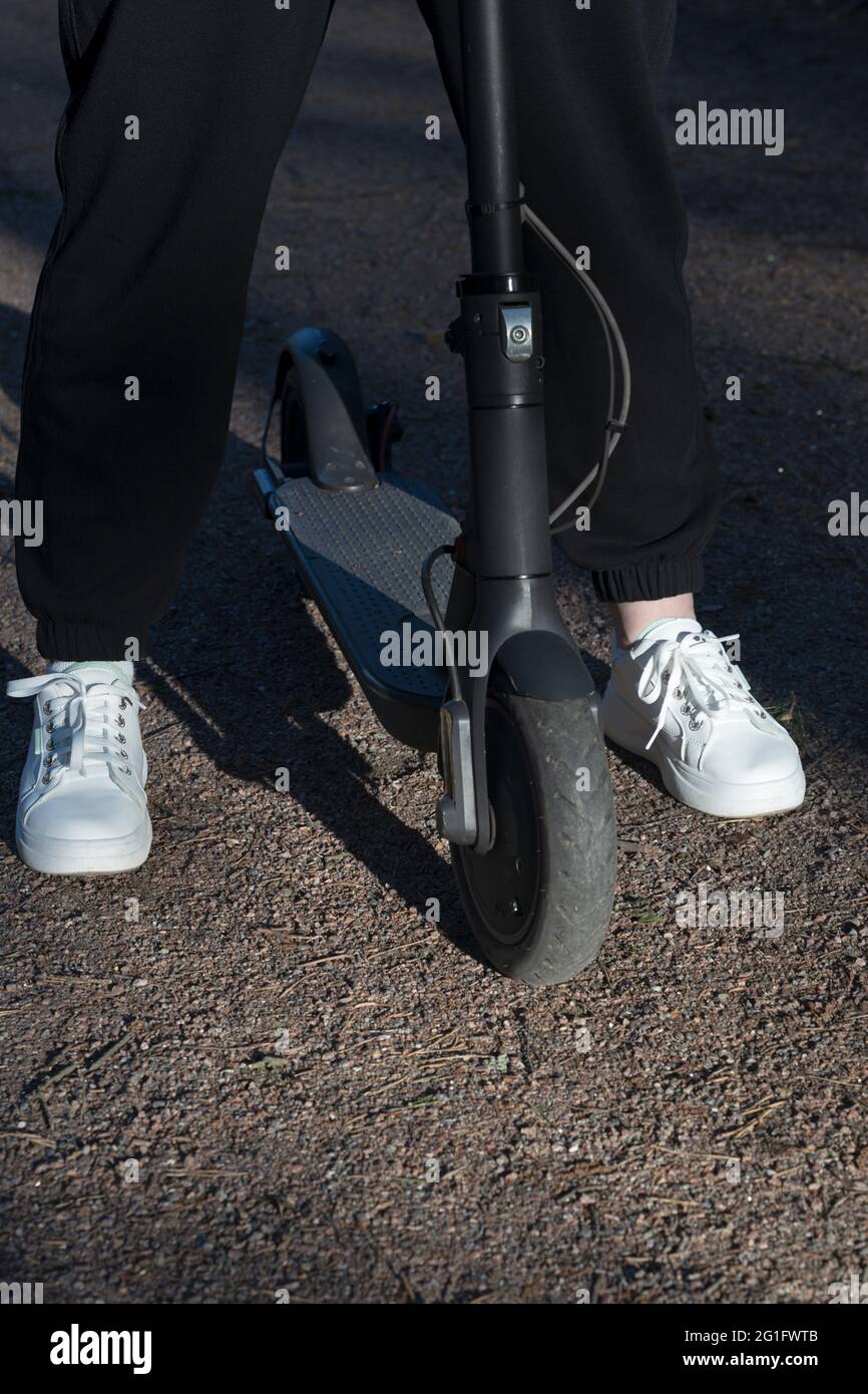 Baskets blanches sur les pieds d'une jeune femme et d'un scooter électrique dans la lumière du soir Banque D'Images