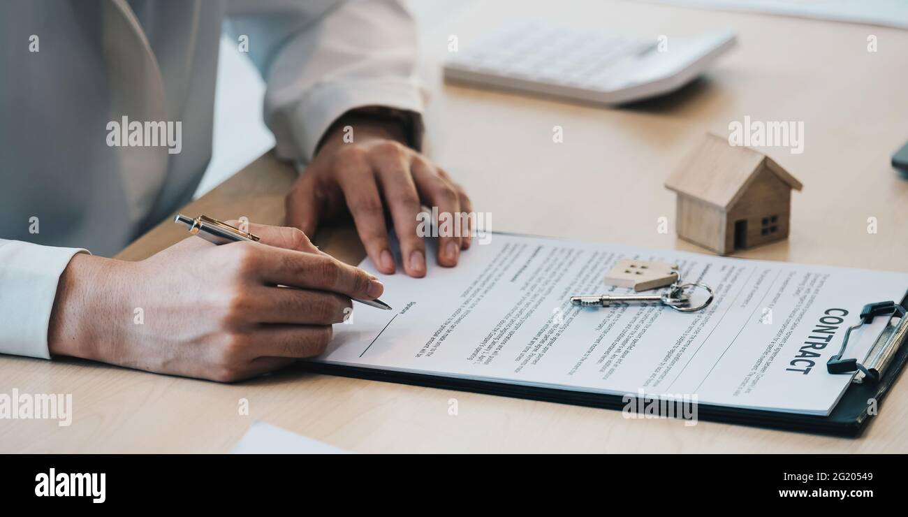 gros plan des mains de femme d'affaires signant les documents de location de maison et avoir une clé d'appartement sur la paperasse Banque D'Images