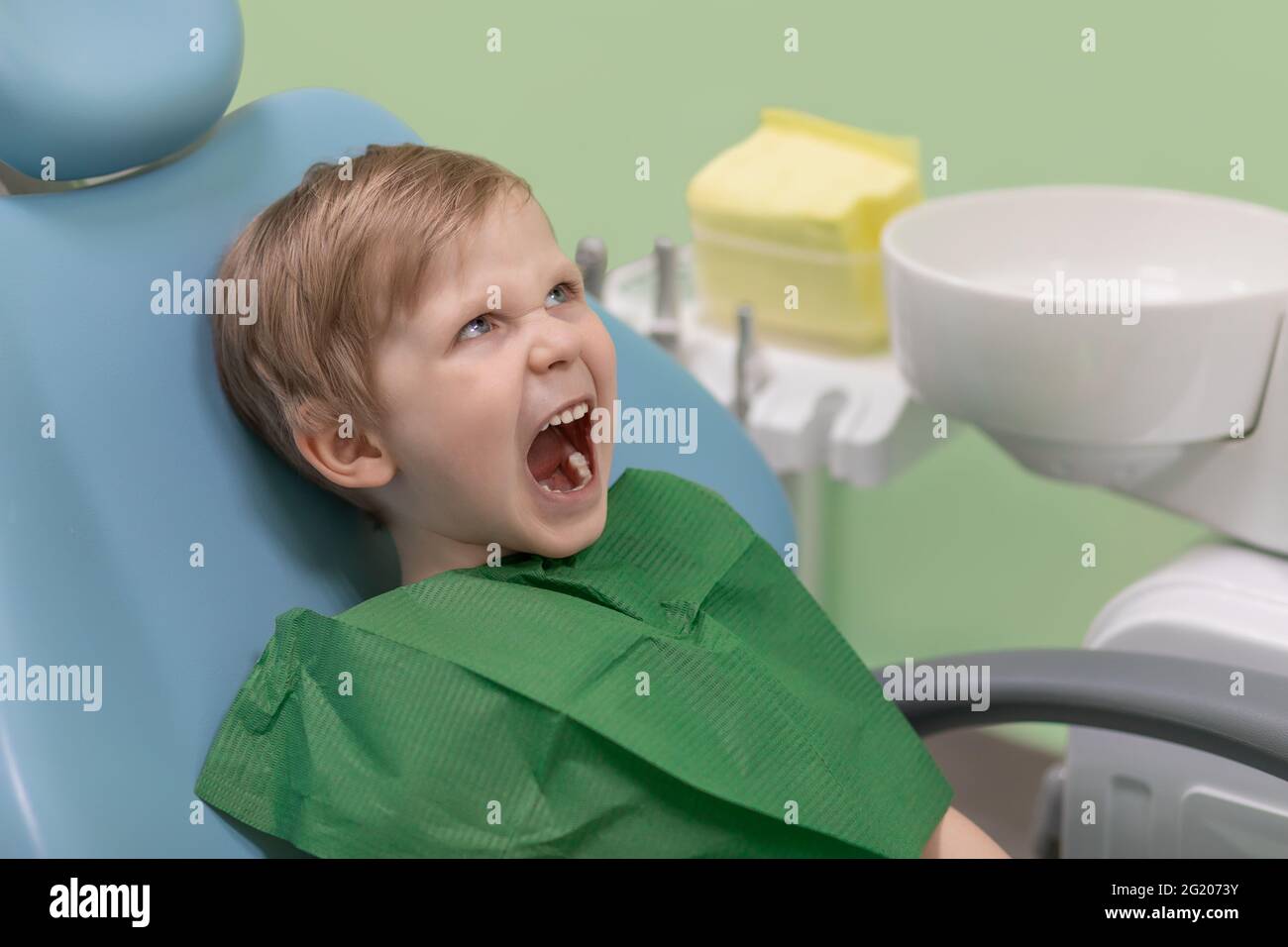 Drôle criant enfant en colère caucasien, a ouvert sa bouche et regarde le dentiste médecin dans la clinique dentaire, en attendant le traitement et l'hygiène buccale. Conc Banque D'Images