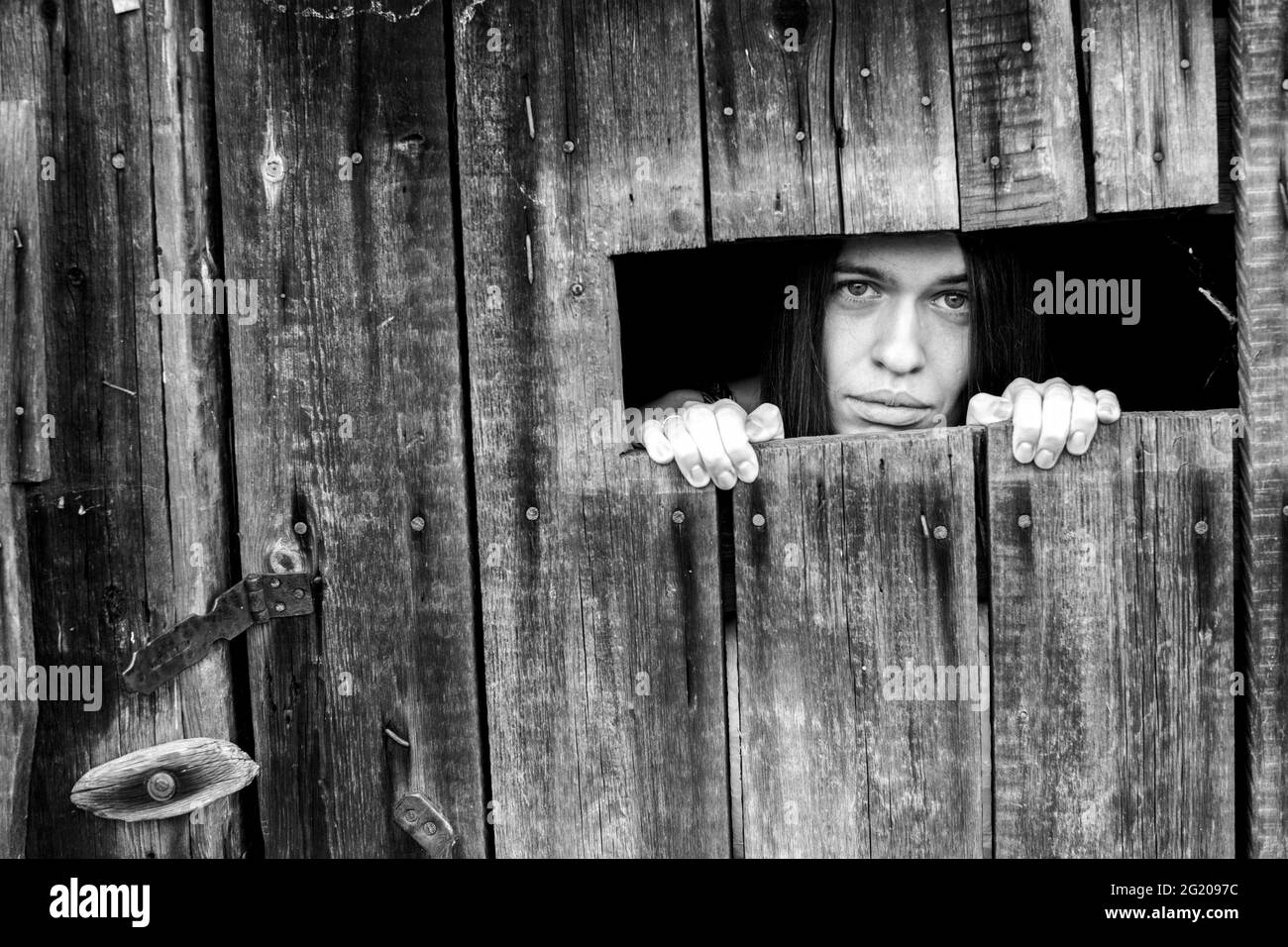 Une femme regardant à travers la fissure d'un hangar en bois verrouillé. Photo en noir et blanc. Banque D'Images