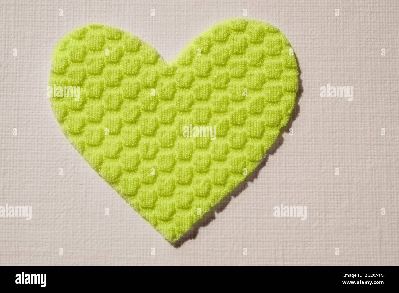 Coeur vert lime en matériau texturé sur une table blanche. Banque D'Images