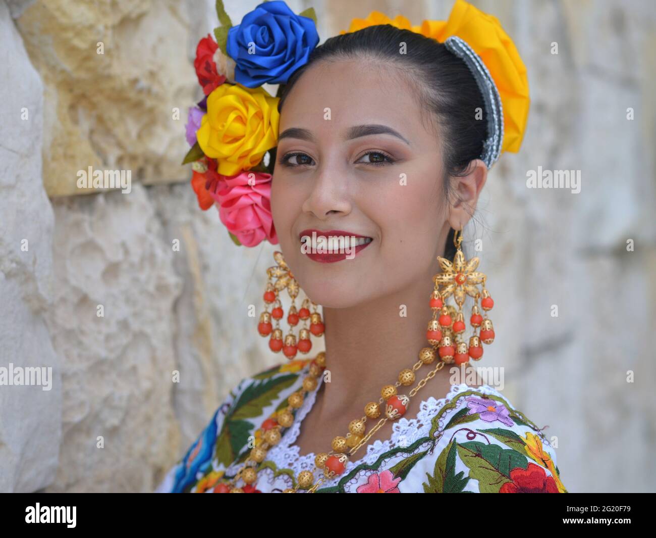 Jeune femme mexicaine belle avec maquillage porte la traditionnelle Yucatecan Yucatecan robe folklorique avec des fleurs dans ses cheveux et sourit pour l'appareil photo. Banque D'Images