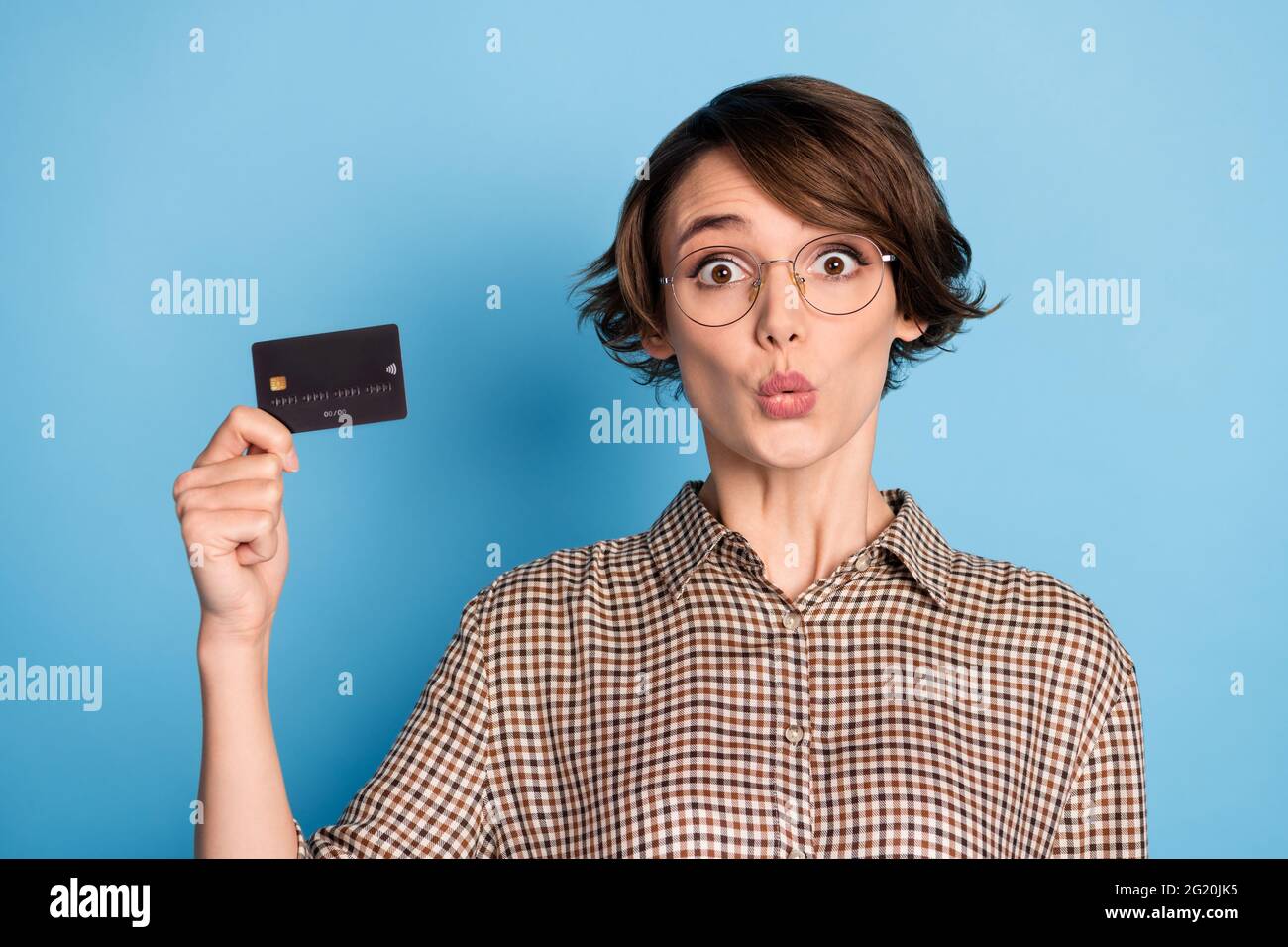 Portrait de la personne choquée main tenir carte de débit regarder l'appareil photo porter damier isolé sur fond bleu Banque D'Images