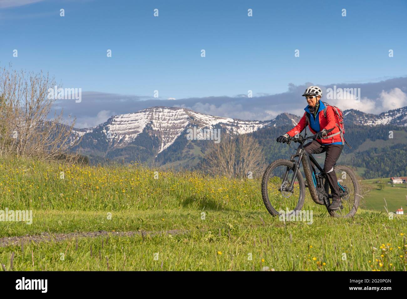 Femme âgée souriante qui monte sur son vélo de montagne électrique sous les montagnes enneigées de la chaîne Nagelfluh près d'Oberstaufen, Allgaeu, Bavière, Allemagne Banque D'Images