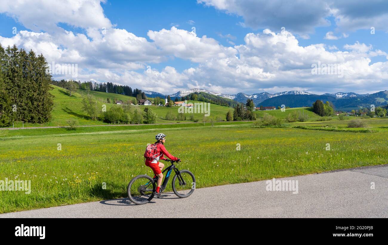 Femme âgée souriante qui monte sur son vélo de montagne électrique sous les montagnes enneigées de la chaîne Nagelfluh près d'Oberstaufen, Allgaeu, Bavière, Allemagne Banque D'Images