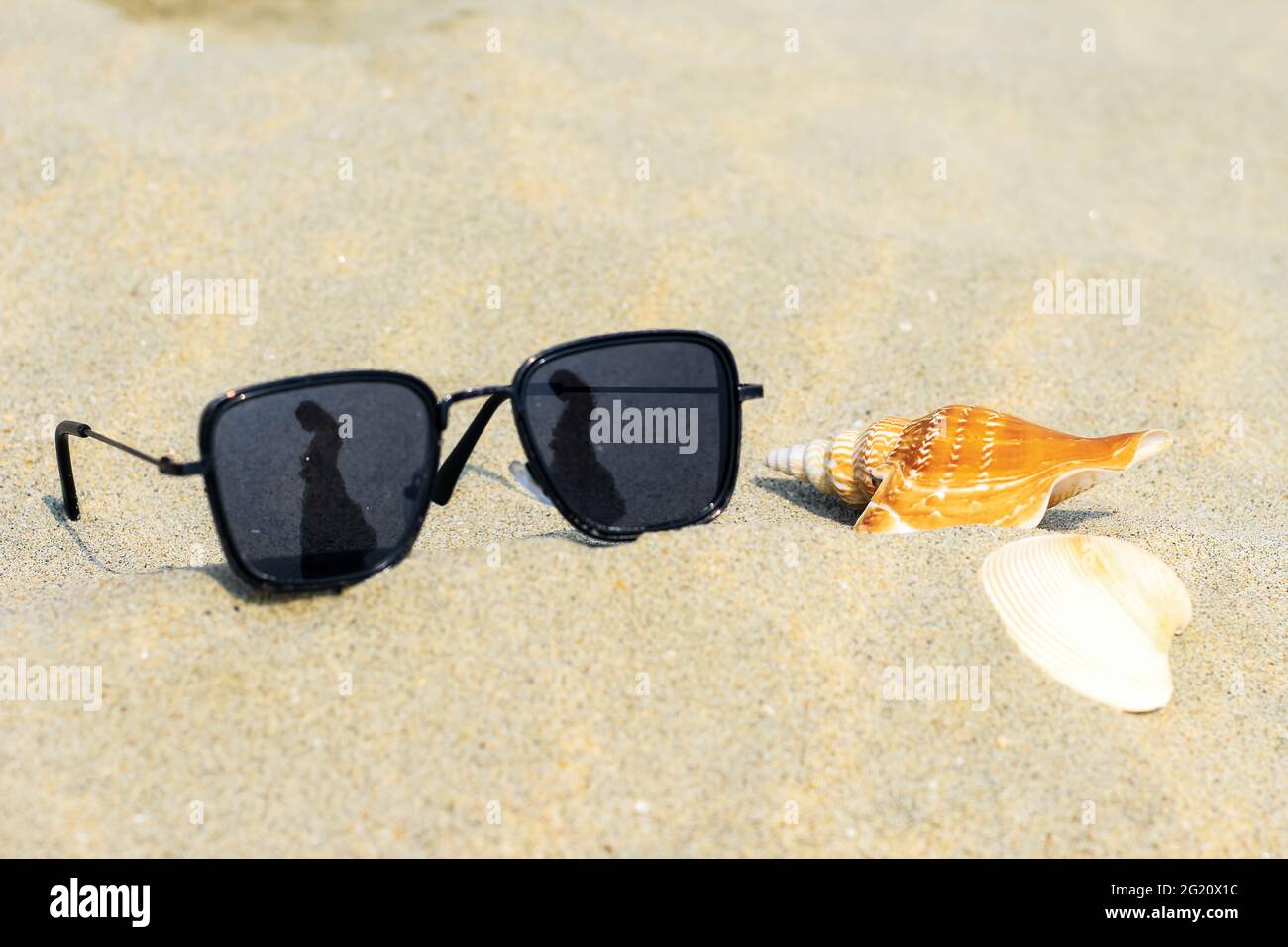 Lunettes de soleil réfléchissantes sur une plage de sable en été, et le  ciel bleu avec une fille se reflète dans des verres avec des coquillages.  Réflexion de la fille sur le