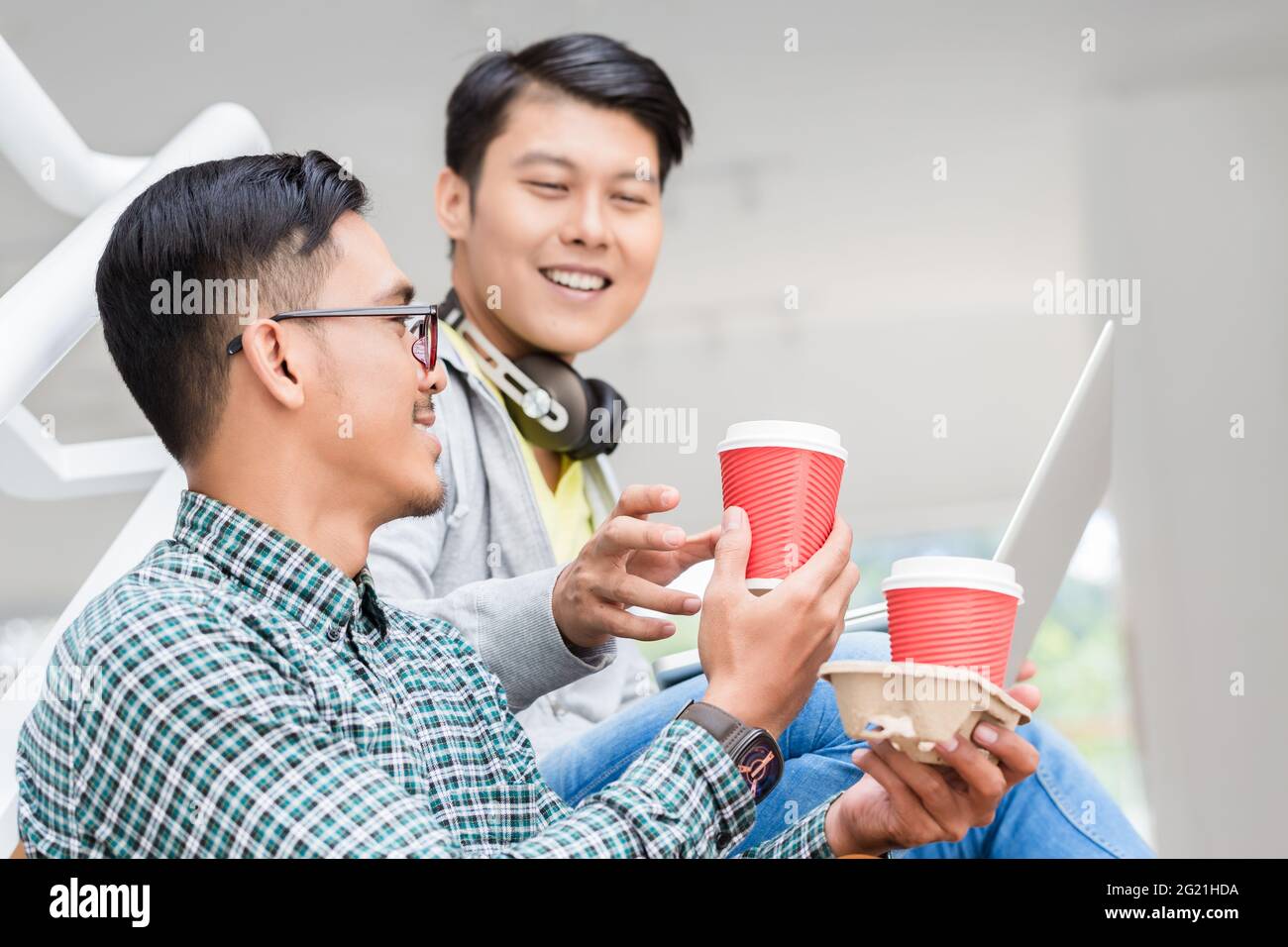 Deux jeunes hommes asiatiques utilisant un ordinateur portable tout en se relaxant pendant faites une pause dans les escaliers d'un bâtiment moderne Banque D'Images