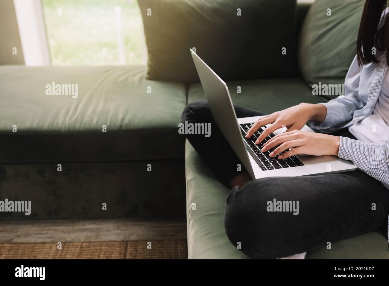 Une fille brune s'assoit sur un canapé vert et imprime ou tape quelque chose sur un ordinateur portable Banque D'Images