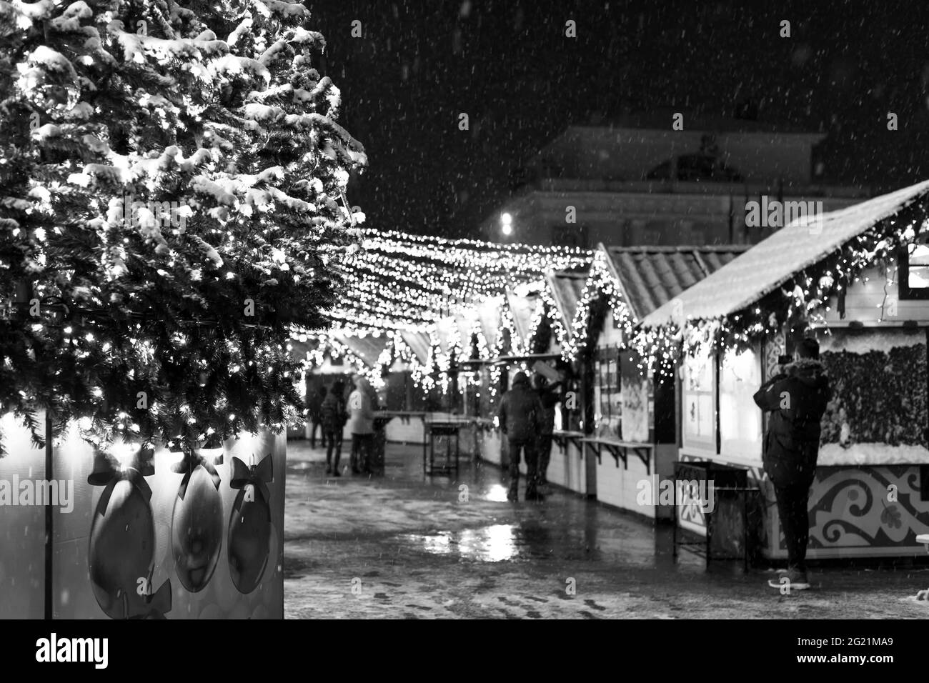 Noël festif et place du nouvel an dans la ville la nuit, chute de neige, arbre du nouvel an et maisons avec guirlandes. Banque D'Images