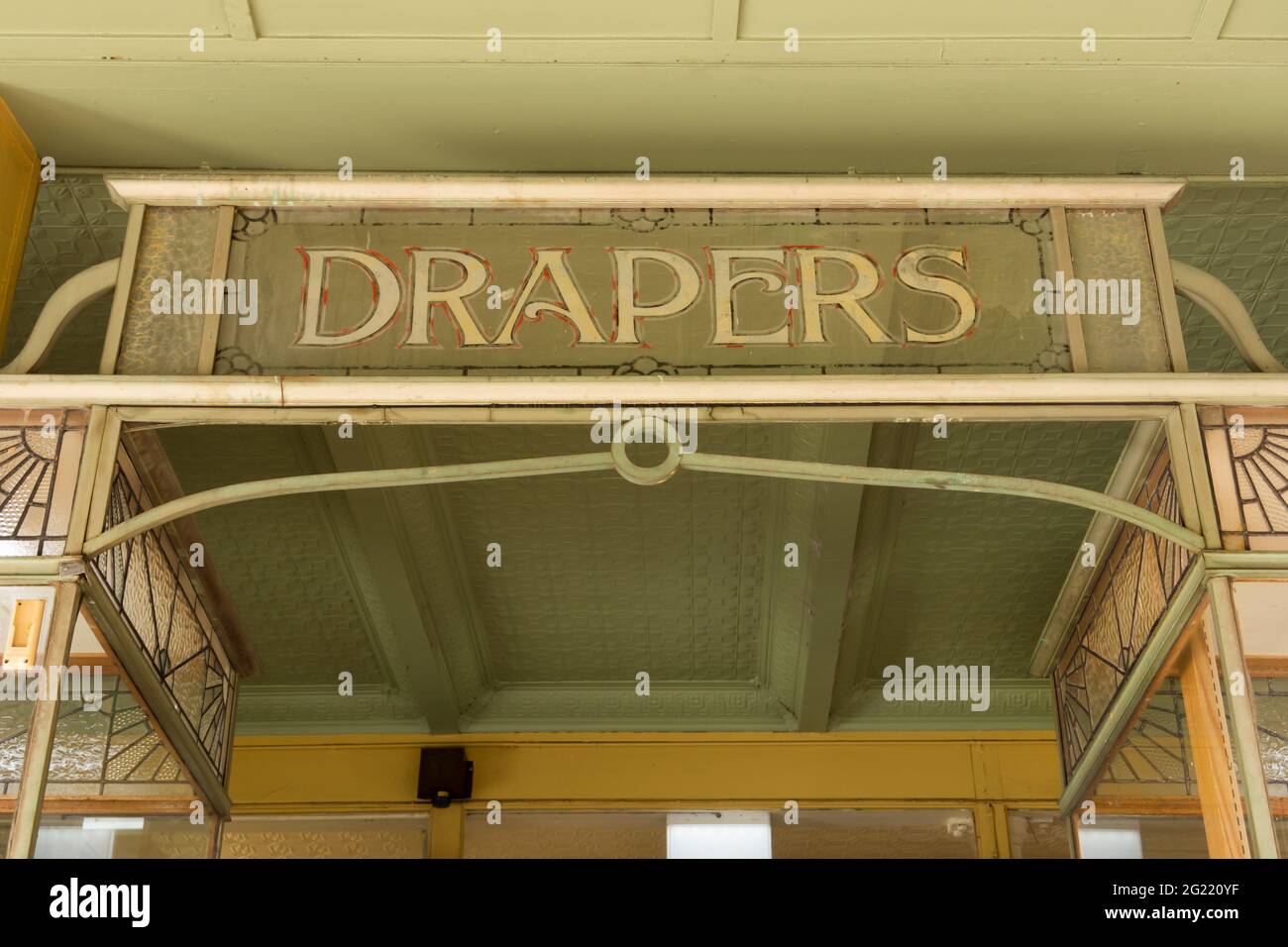 Affiche rétro vintage art déco drapers sur l'avant de l'ancien magasin avec incrustations en verre fantaisie et plafond en étain pressé. Banque D'Images