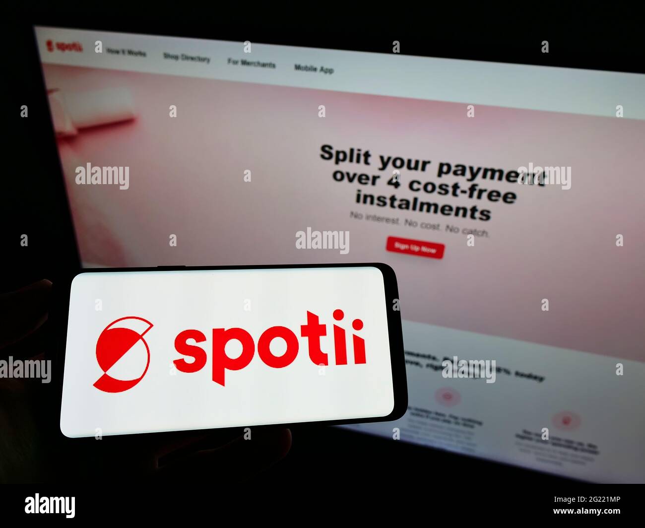 Personne tenant un téléphone mobile avec le logo de la société de plateforme de paiement Spotii DMCC sur l'écran en face de la page Web d'affaires. Mise au point sur l'affichage du téléphone. Banque D'Images